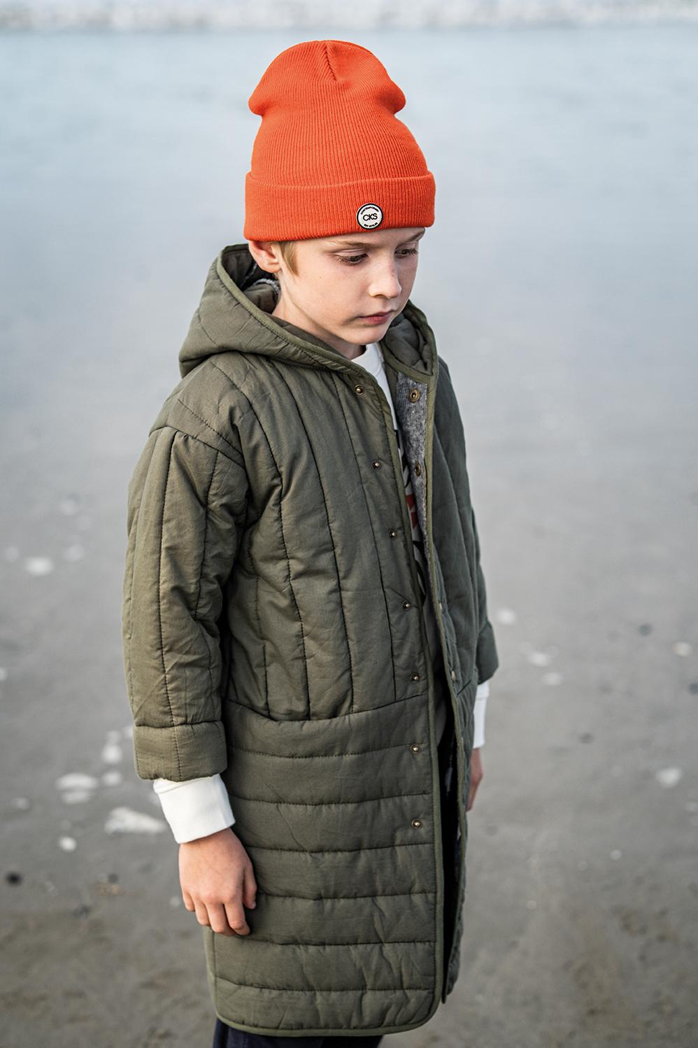 Child wearing the Child/Teen Bobby Jacket sewing pattern from Fibre Mood on The Fold Line. A jacket pattern made in padded, quilted, matelassé, faux fur, teddy or wool fabrics, featuring front snap fasteners, coat length, hood and full length sleeves.