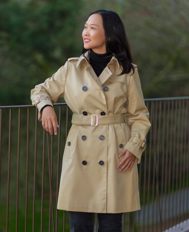 Woman wearing the Acari Trench Coat sewing pattern from Itch to Stitch on The Fold Line. A coat pattern made in gabardine, woollen, boiled wool, or non-stretch fleece fabric, featuring a double-breasted front, two-piece sleeves, back vent, gun flap, storm flap, epaulettes, sleeve bands, buttoned welt pockets, and full lining.