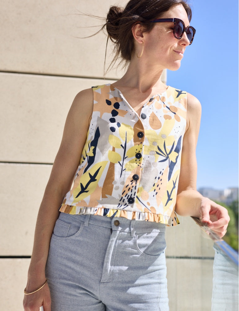 Woman wearing the Archipel Top sewing pattern from Atelier Scämmit on The Fold Line. A sleeveless top pattern made in silk, viscose, or linen fabric, featuring a round neckline, front button placket, and hem ruffle.