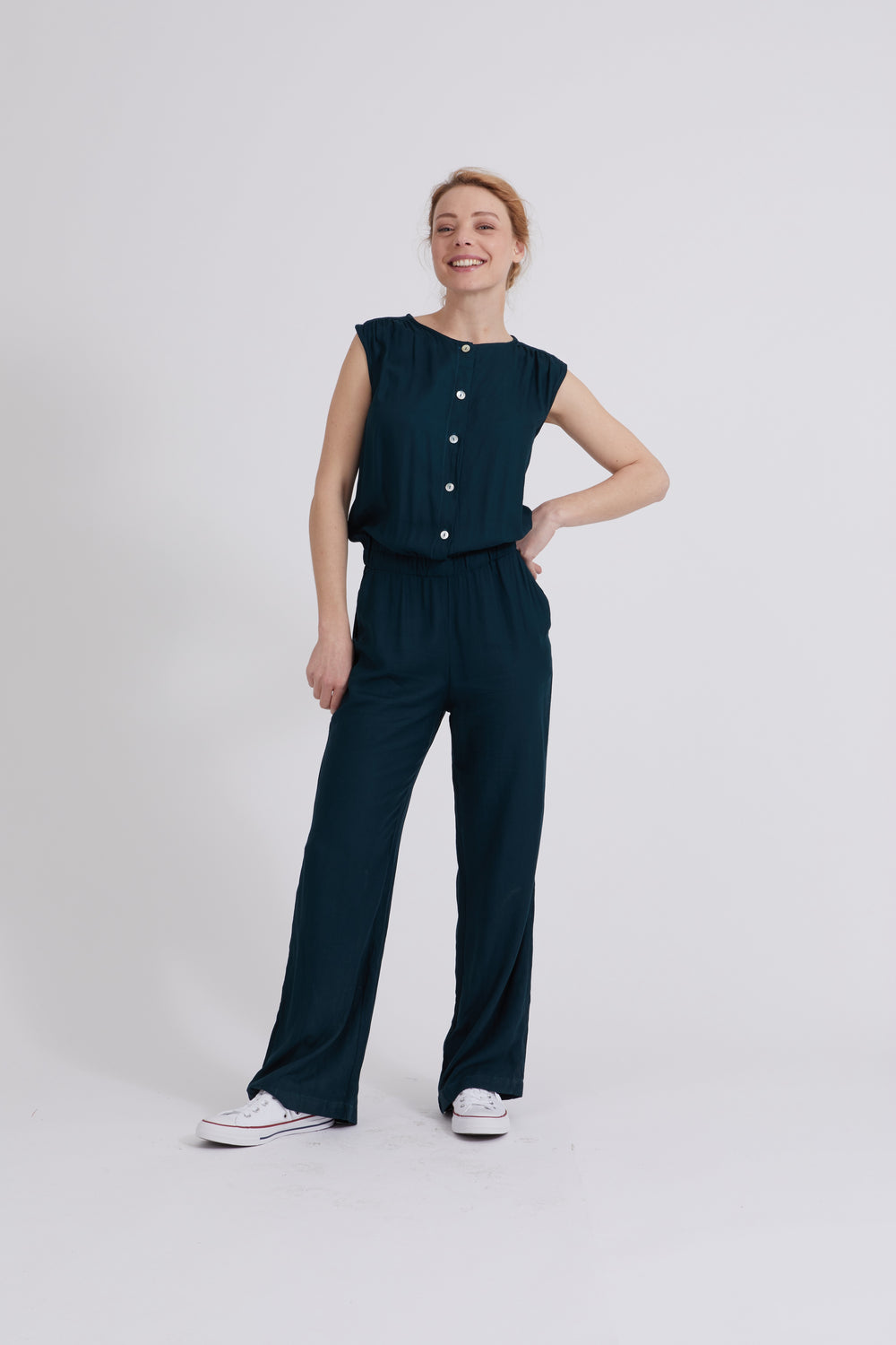 Woman wearing the Astrid Jumpsuit sewing pattern from Coralie Bijasson on The Fold Line. A sleeveless jumpsuit pattern made in viscose, crepe, linen, light wool, chambray or cotton fabric, featuring a round neckline, gathers at the shoulders, a button front, elasticated waist, and straight legs.