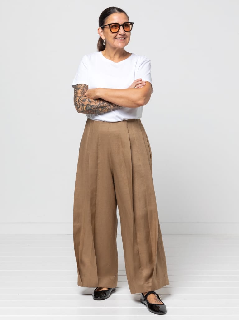 Woman wearing the Atlas Woven Pant sewing pattern from Style Arc on The Fold Line. A trousers pattern made in cotton, linen, or denim fabric, featuring a wide leg, fitted waist, slightly dropped crotch, statement twisted pleat detail, and side seam pockets.