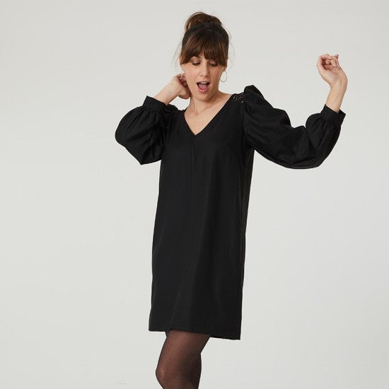 Woman wearing the Auriane Dress sewing pattern from Coralie Bijasson on The Fold Line. A dress pattern made in voile, crepe, wool suiting, cotton, milano jersey, or chambray fabric, featuring a V-neckline, shoulder yokes, long puff sleeves with cuffs, and above knee length.