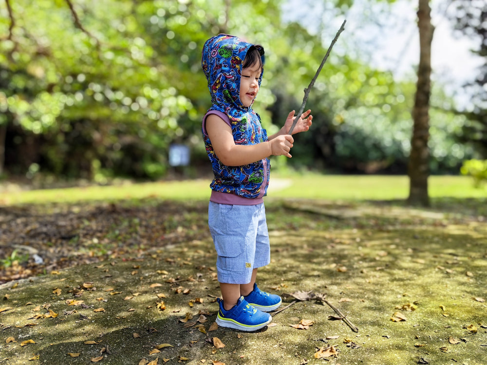Boy wearing the Baby/Child Milkshake Hoodie sewing pattern from Waves & Wild on The Fold Line. A sleeveless top pattern made in knit fabric, featuring a hood, front pocket, and rib trim.