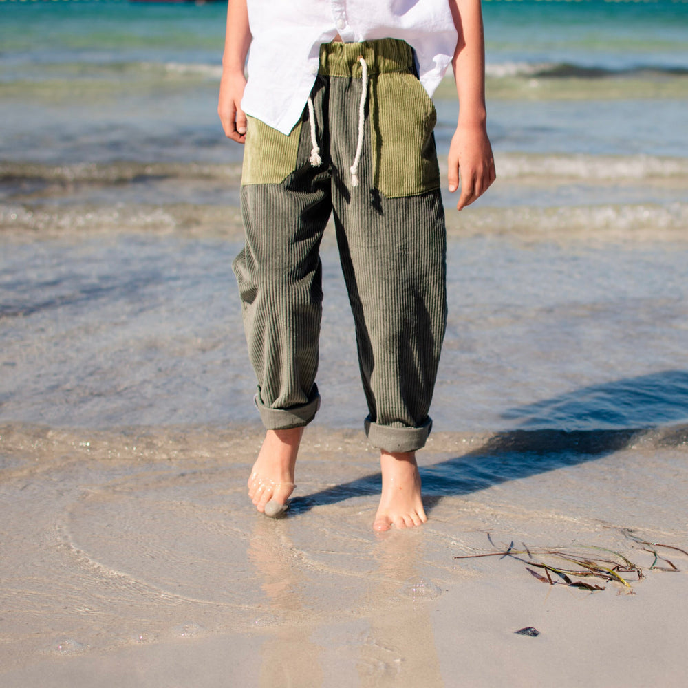 Boy wearing the Baby/Child Sunday Pants sewing pattern from Waves & Wild on The Fold Line. A trousers pattern made in corduroy, wool, denim, linen, or double gauze fabric, featuring an elastic waist, drawstring, patch pockets, dropped crotch, tapered legs, and rolled cuffs.