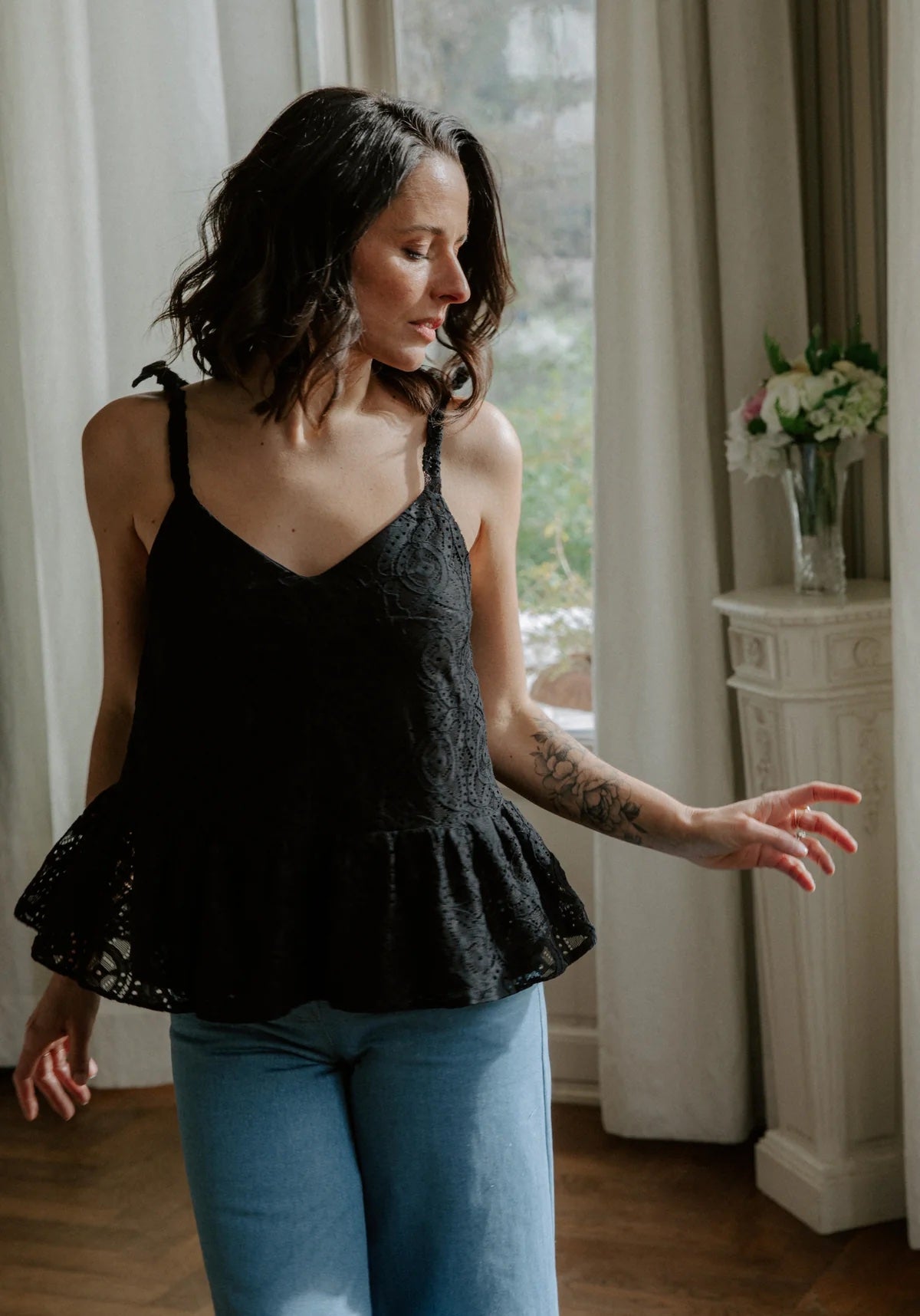 Woman wearing the Belle Épine Top sewing pattern from Maison Fauve on The Fold Line. A top pattern made in viscose, tencel, cotton, crepe, poplin, satin, twill, or lace fabric, featuring radiating bust darts, V-necklines at the front and back, tie straps, and a gathered peplum.