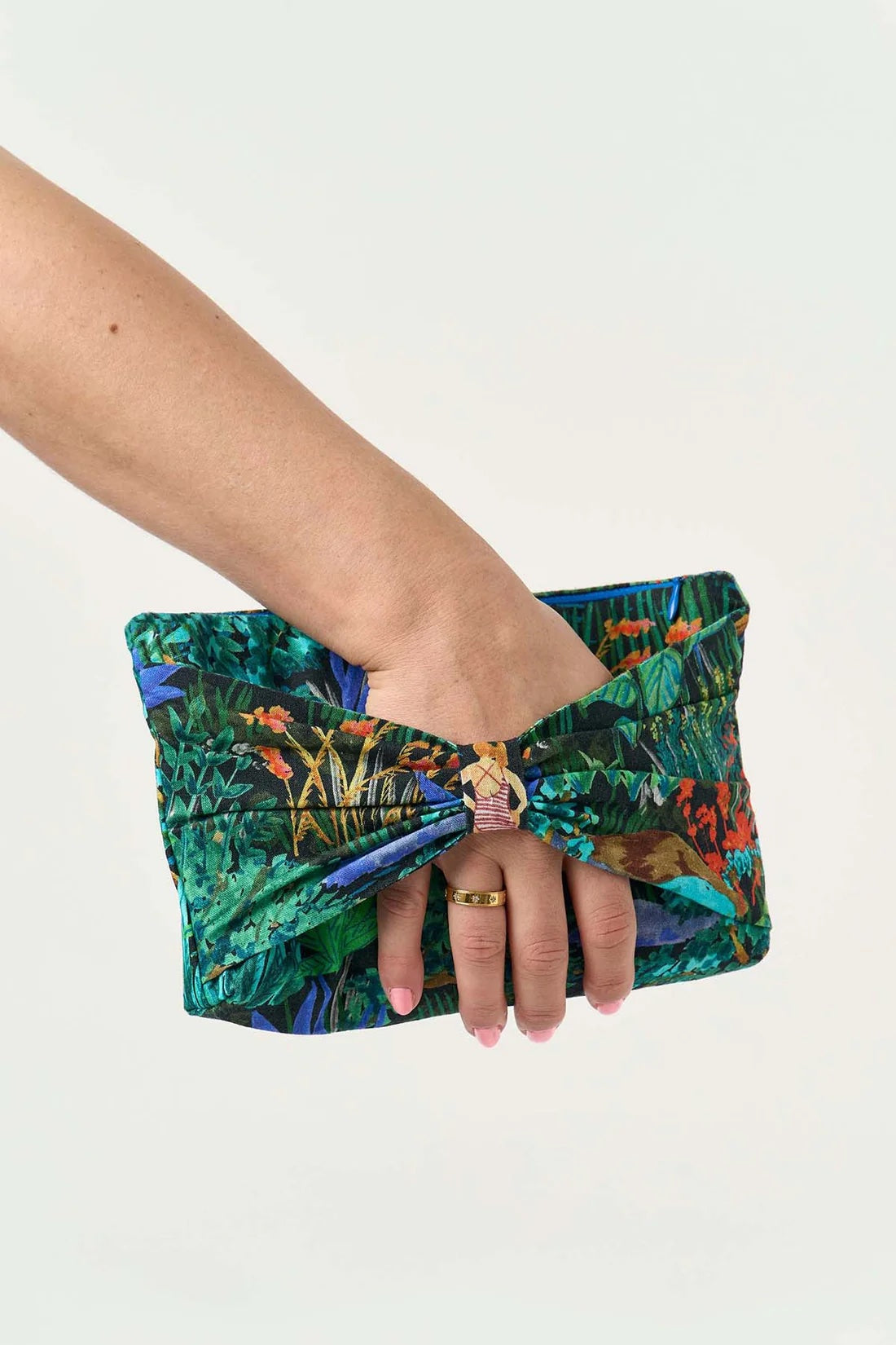 Woman holding the Bow Bag sewing pattern from Sew Over It on The Fold Line. A clutch bag pattern made in viscose, linen, or cotton fabric, featuring a rectangular shape, full lining, boxed bottom, zipper closure, and front bow.