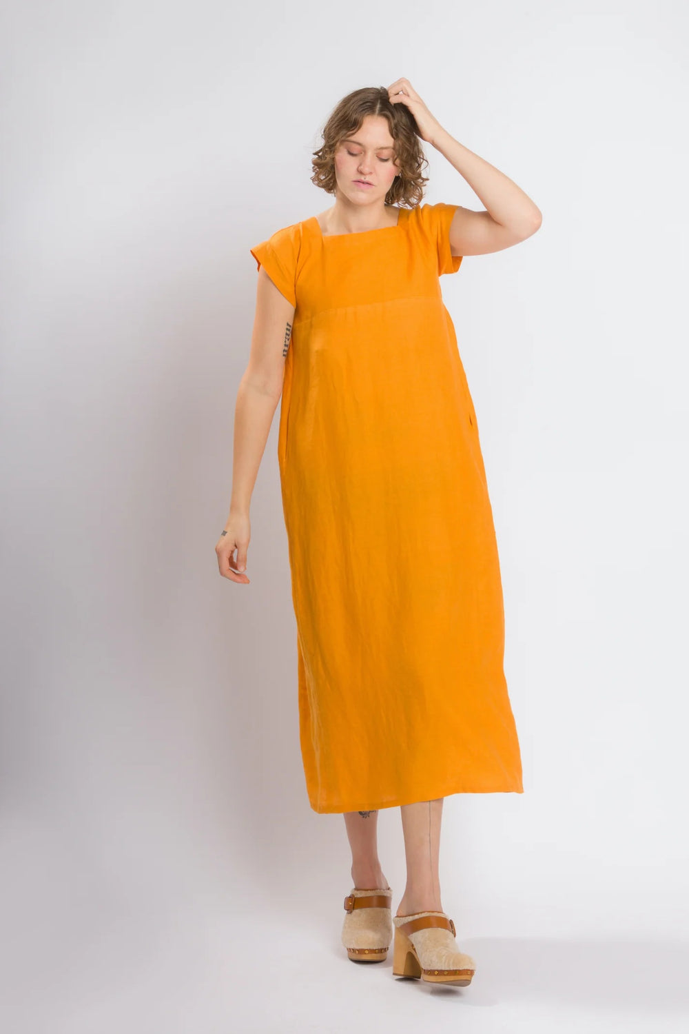 Woman wearing the Casita Dress sewing pattern from Cris Wood Sews on The Fold Line. A dress pattern made in linen, lightweight cotton, silk, rayon, viscose blend, or gauze fabric, featuring a square neckline, front and back yokes, short grown-on sleeves, side seam pockets, and a midi length.