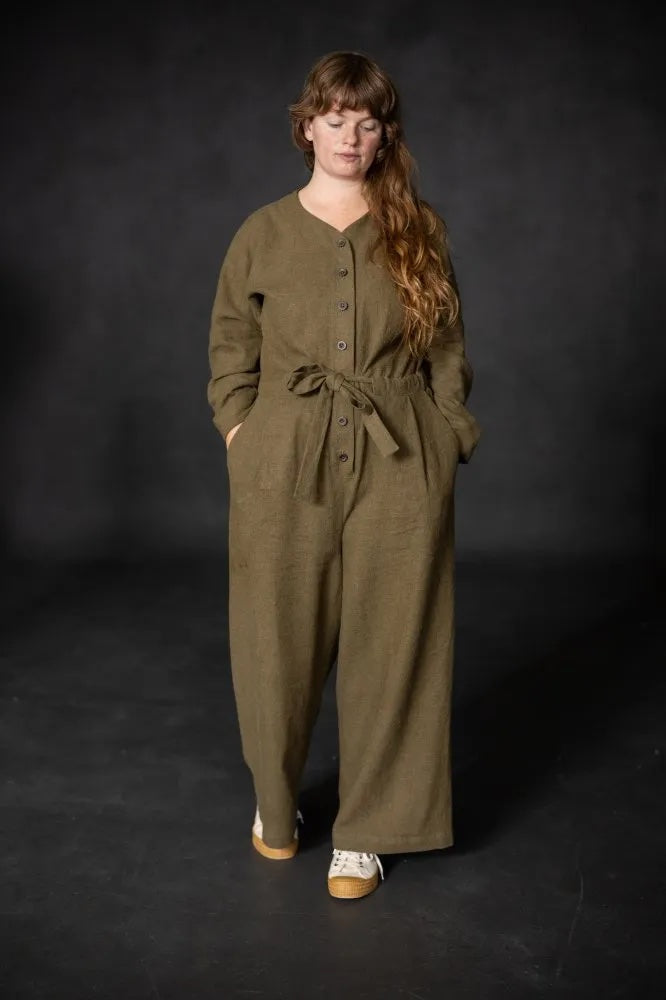 Woman wearing the Cassidy Jumpsuit sewing pattern from Merchant & Mills on The Fold Line. A jumpsuit pattern made in twill, denim, linen, cotton poplin, tencel, or corduroy fabric, featuring a relaxed fit, long sleeves, button front, waist tie, elasticated back waist, wide legs, and pockets.