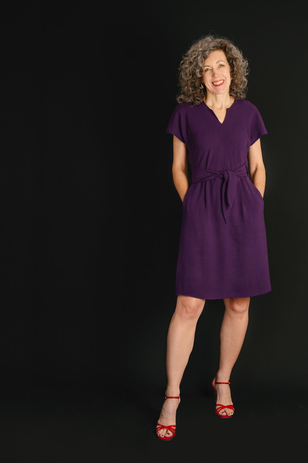 Woman wearing the Chacarita Wrap Dress sewing pattern from Liesl + Co on The Fold Line. A dress pattern made in linen, rayon, or soft cotton fabric, featuring a bias-cut top with a notch at the front neck, short sleeves, ties at the front waist, on-seam pockets, a V-neck at the back, and knee length.