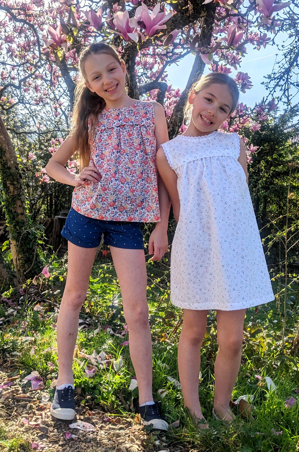 Girls wearing the Child/Teen Celesta Top or Dress sewing pattern from Petits D'om on The Fold Line. A top or dress pattern made in batiste, viscose, Liberty, cotton voile, poplin, double gauze, or tencel fabric, featuring a rounded neckline at the front, v-neckline at the back, horizontal pleat above the bust with gathers underneath, and optional lace trim.