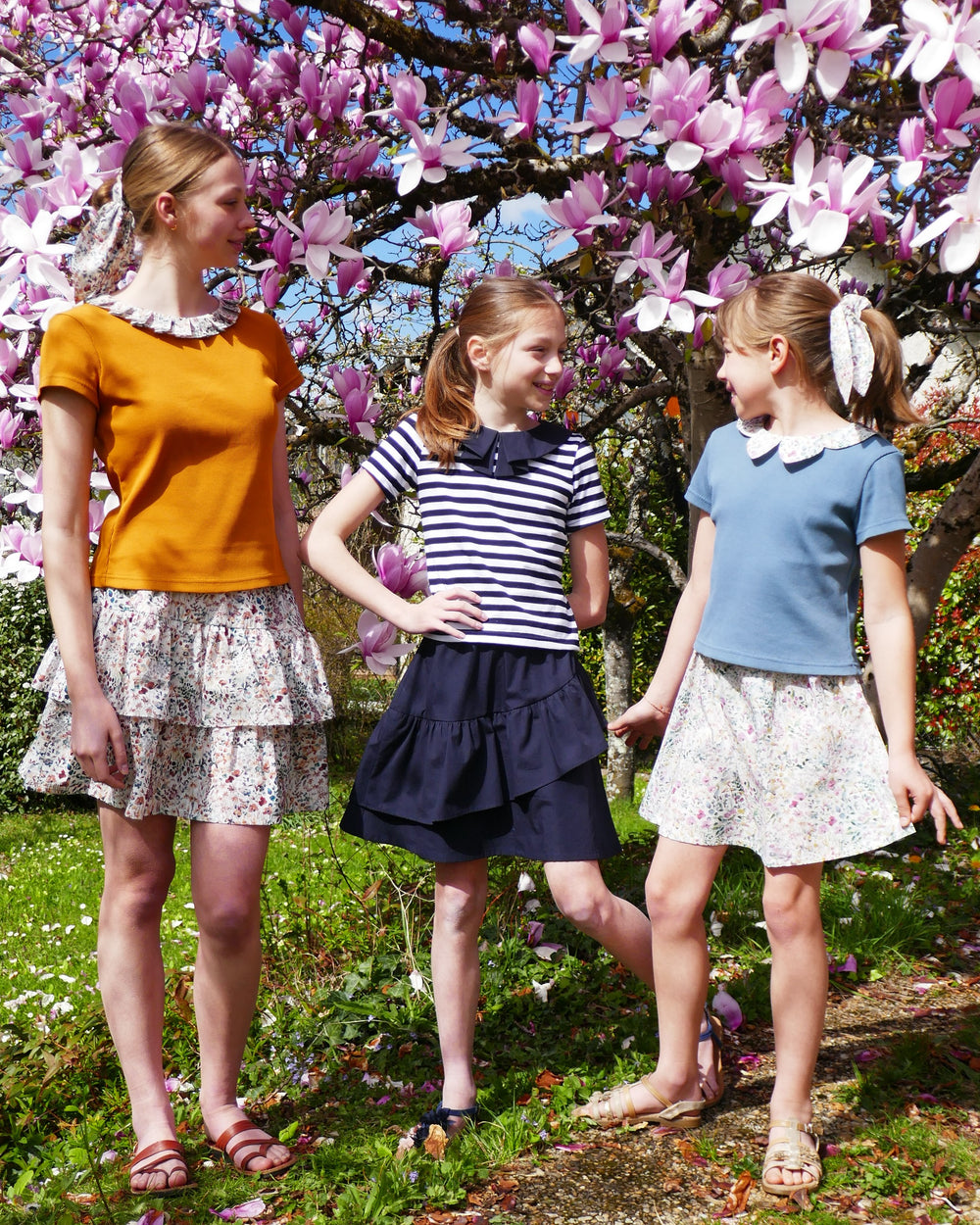 Girls wearing the Child/Teen Flores Skirt sewing pattern from Petits D'om on The Fold Line. A skirt pattern made in Liberty lawn, batiste, plumetis, cotton voile, or viscose fabric, featuring an elastic waist and optional ruffles.