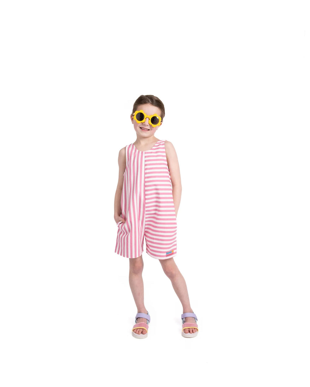 Girl wearing the Child/Teen Folly Jumpsuit sewing pattern from Little Rosy Cheeks on The Fold Line. A playsuit pattern made in cotton, denim, needlecord, linen, double gauze, or viscose fabric, featuring a bias bound neckline and armholes, elasticated back, and side pockets.