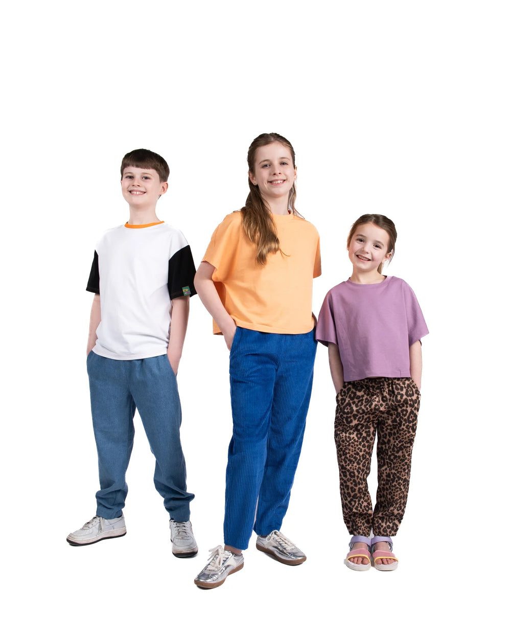Children wearing the Child/Teen Innis Trousers sewing pattern from Little Rosy Cheeks on The Fold Line. A pants pattern made in denim, corduroy, cotton twill, linen, or canvas fabric, featuring an elasticated waist, back yoke, pockets, front hem darts, and barrel leg.