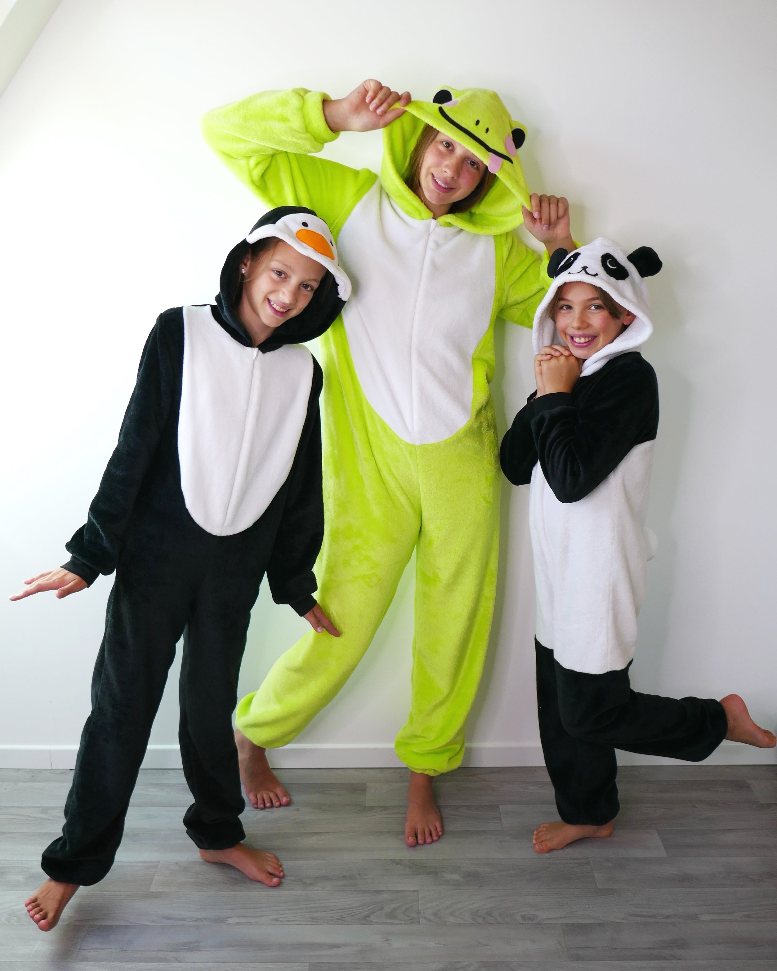 Children wearing the Child/Teen Nocturne Onesie sewing pattern from Petits D'om on The Fold Line. A pyjama pattern made in lightweight fluffy fleece or double-sided microfleece fabric, featuring a front zipper, optional pockets, and hood with a panda, penguin or frog design.