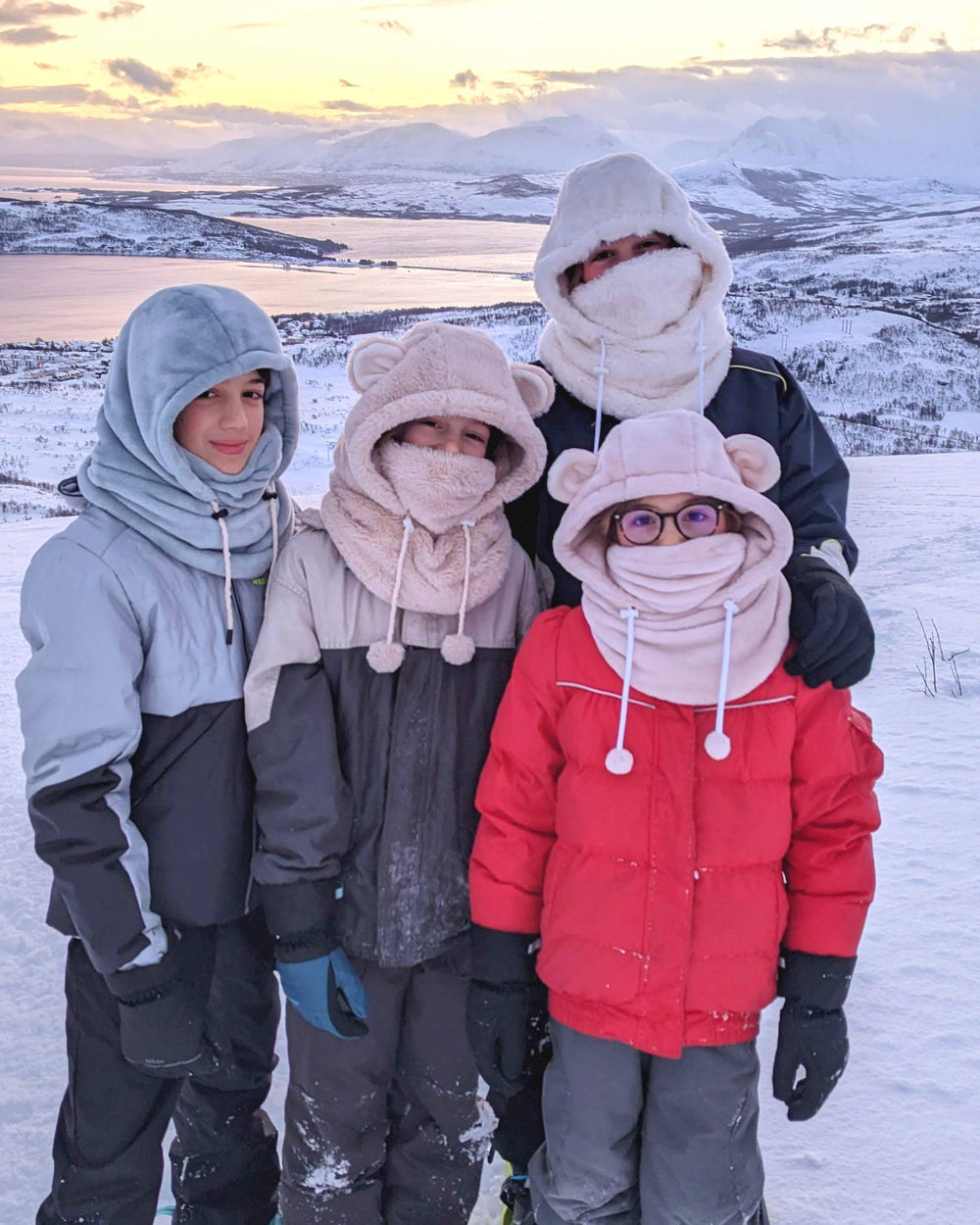 Children wearing the Child/Teen Nordic Snood or Hood sewing pattern from Petits D'om on The Fold Line. A snood pattern made in cuddle fleece, faux fur, or sherpa fabric, featuring a hood with a drawstring and optional bear ears.