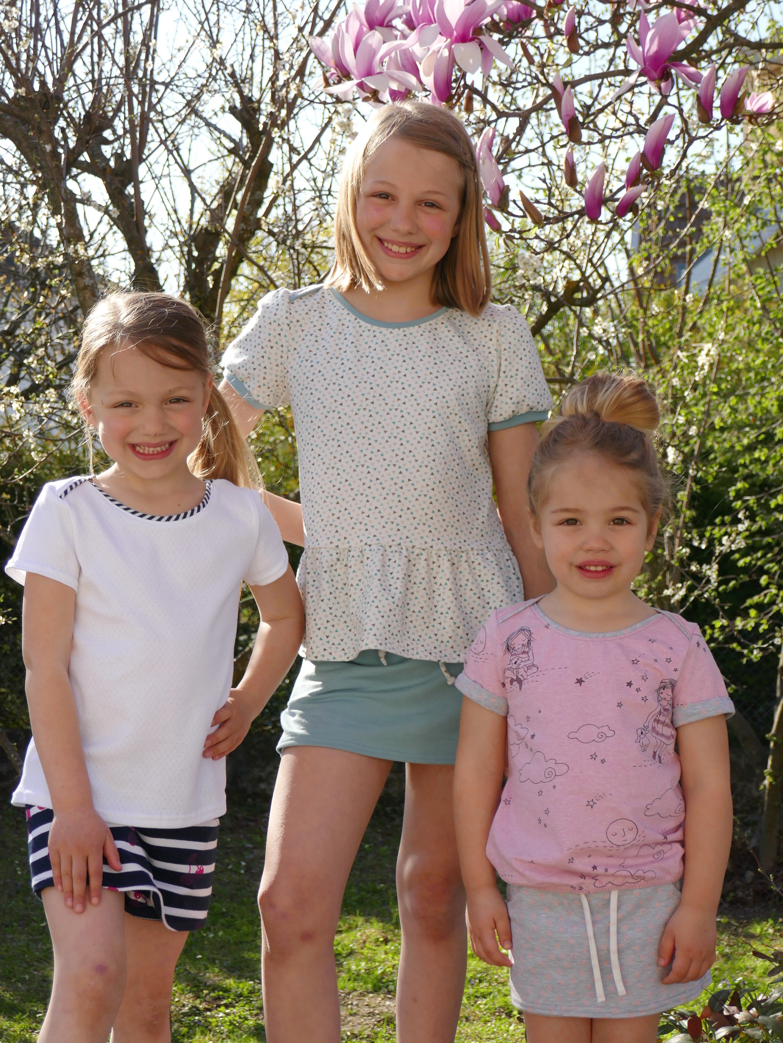 Girls wearing the Child/Teen Sohel T-shirt sewing pattern from Petits D'om on The Fold Line. A T-shirt pattern made in jersey knit fabric, featuring an envelope neckline, short sleeves, and options for a classic hem, elasticated hem or peplum.