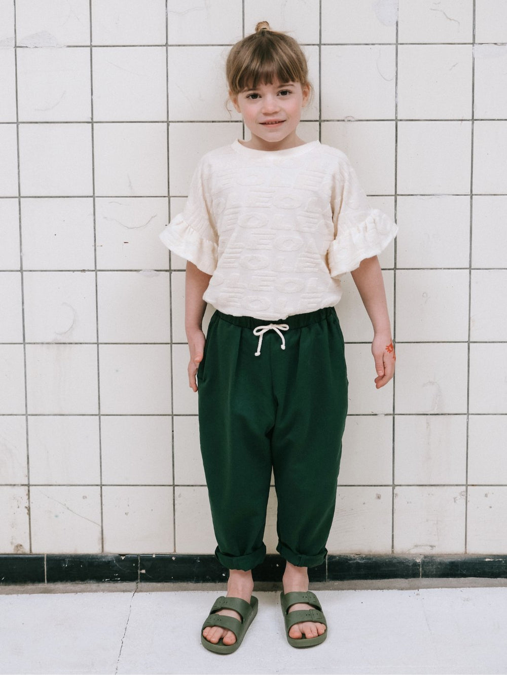 Girl wearing the Child/Teen Willy Top sewing pattern from Notches on The Fold Line. A top pattern made in jersey or woven fabric, featuring a round neck, dropped shoulders, and short sleeves with ruffles.