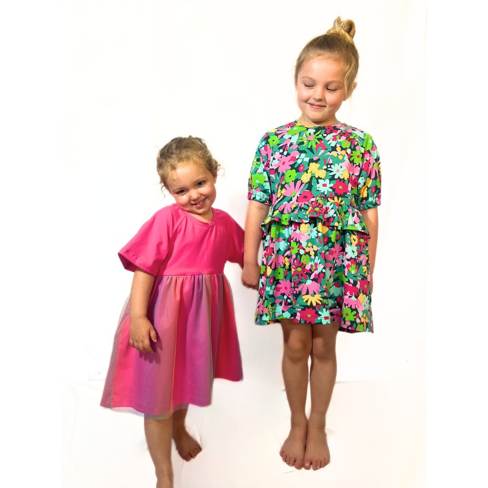 Girls wearing the Children's Devon Jersey Smock Dress sewing pattern from Pattern Paper Scissors on The Fold Line. A dress pattern made in jersey, knit, or cotton elastane fabric, featuring a loose fit, round neckline, puff or flared short sleeves, an optional waist frill, and optional tulle skirt layer.