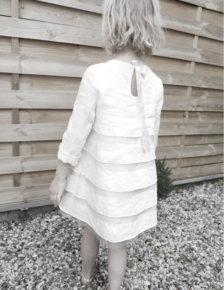 Girl wearing the Children's Petite Fee Dress sewing pattern from Atelier Scämmit on The Fold Line. A dress pattern made in batiste or double gauze fabric, featuring a slightly flared silhouette, flounces, and a keyhole back opening with ties.