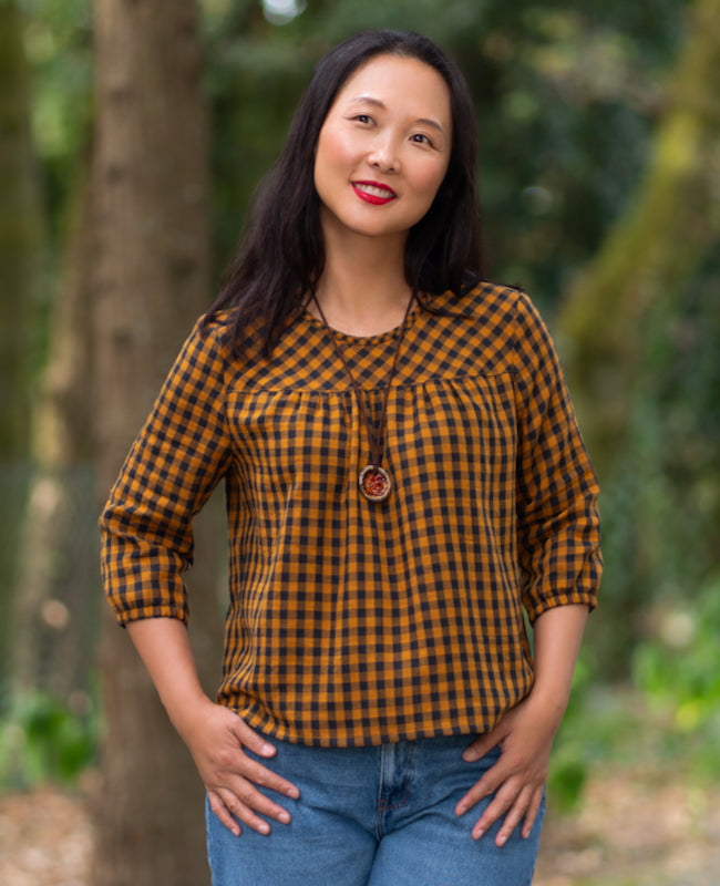 Woman wearing the Clemente Top sewing pattern from Itch to Stitch on The Fold Line. A top pattern made in shirting, rayon challis, batiste, chambray, lightweight linen, double gauze, or lightweight broadcloth fabric, featuring a round bias-bound neckline, front and back yokes with gathers, and 3/4 length sleeves.