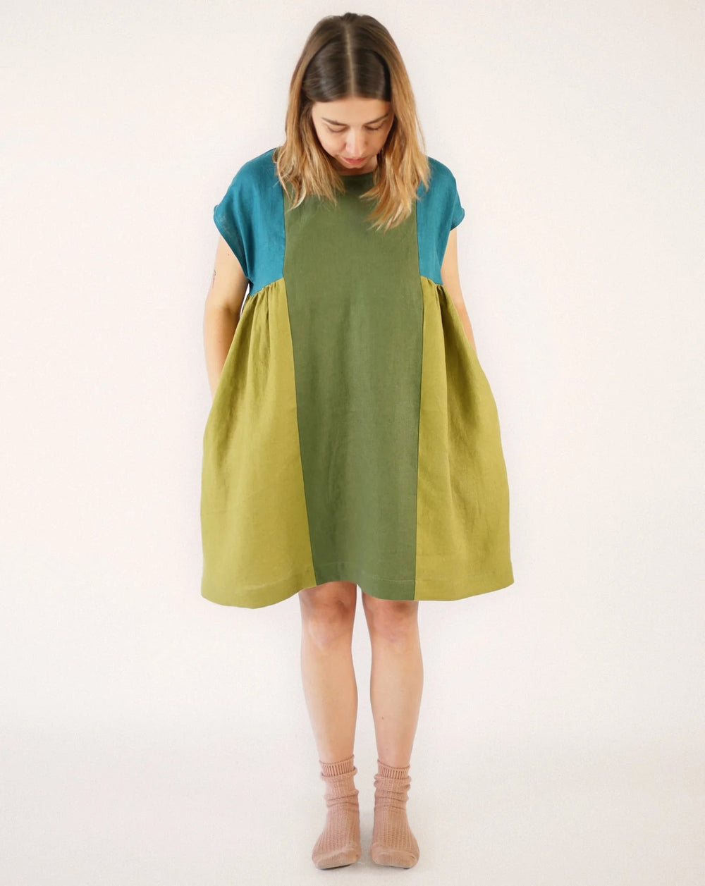 Woman wearing the Collage Gather Dress sewing pattern from Matchy Matchy Sewing Club on The Fold Line. A dress pattern made in light to medium weight woven fabric, featuring a relaxed boxy fit, round neckline, grown-on short sleeves, side gathers, in-seam pockets, and knee length.