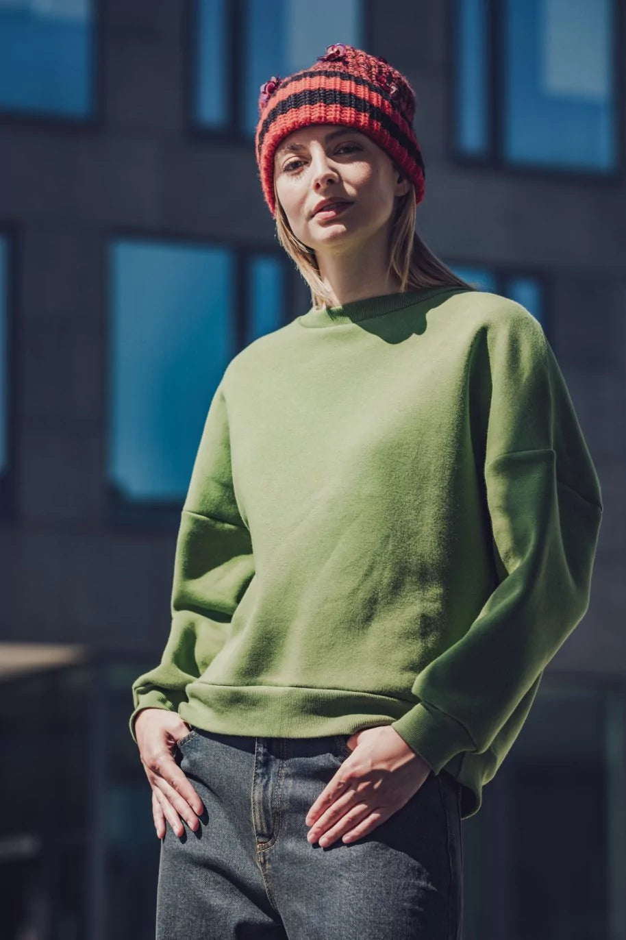 Woman wearing the Chicku Sweater sewing pattern from Fibre Mood on The Fold Line. A sweatshirt pattern made in sweatshirt, French terry, neoprene, knitted jacquard, or ponte Roma fabric, featuring an oversized fit, round neck, long sleeves, rib trim, and cut-out at the back.