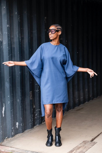 Woman wearing the Dallas Dress sewing pattern from Fibre Mood on The Fold Line. A dress pattern made in fabric with good drape, featuring a round neckline, above knee length, and rectangular back panel that creates an elegant cape effect.