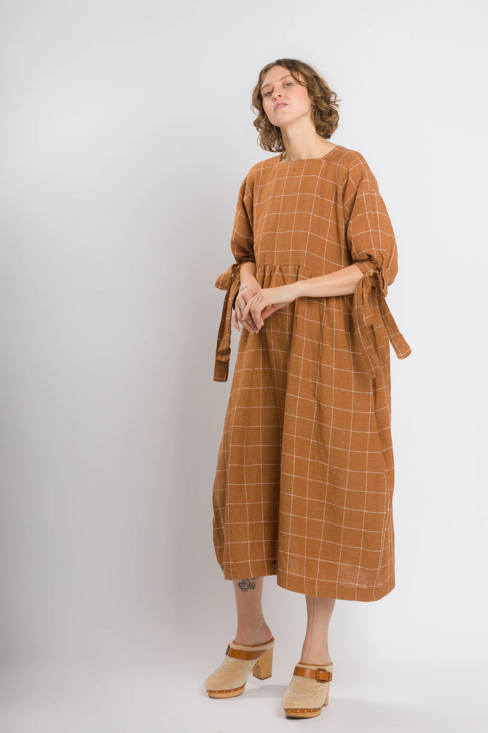 Woman wearing the Daydream Dress sewing pattern from Cris Wood Sews on The Fold Line. A dress pattern made in linen, lightweight cotton, silk, rayon, viscose blend, or gauze fabric, featuring a square neckline, mid-length sleeves with bows, and a midi length.