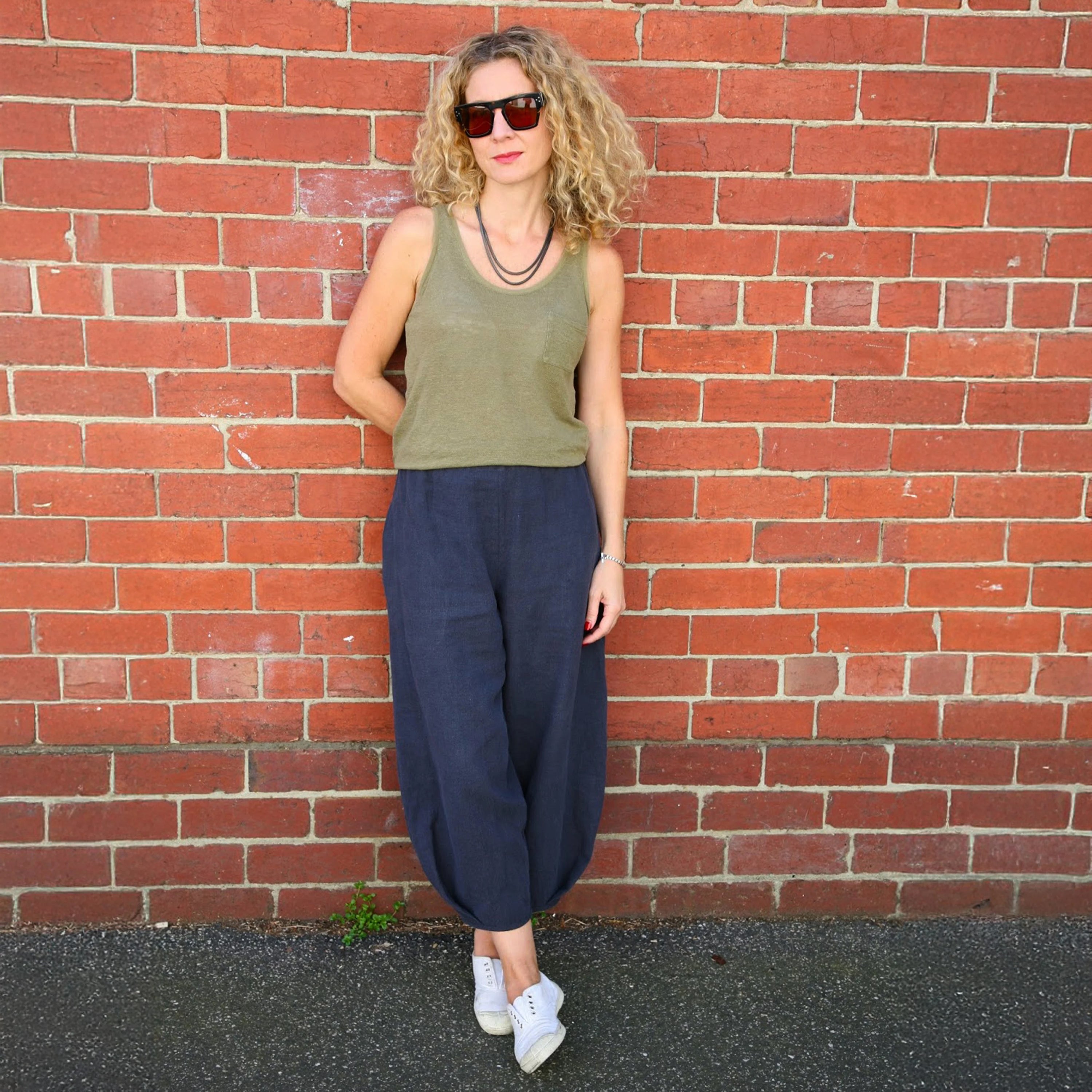 Woman wearing the Demi Pants sewing pattern from Tessuti Fabrics on The Fold Line. A pants pattern made in linen, lightweight wool, cotton, viscose, silk faille or crepe fabric, featuring an elasticised waist, full legs, stitched-down side pockets, and a pleat detail at the front and back hemline.