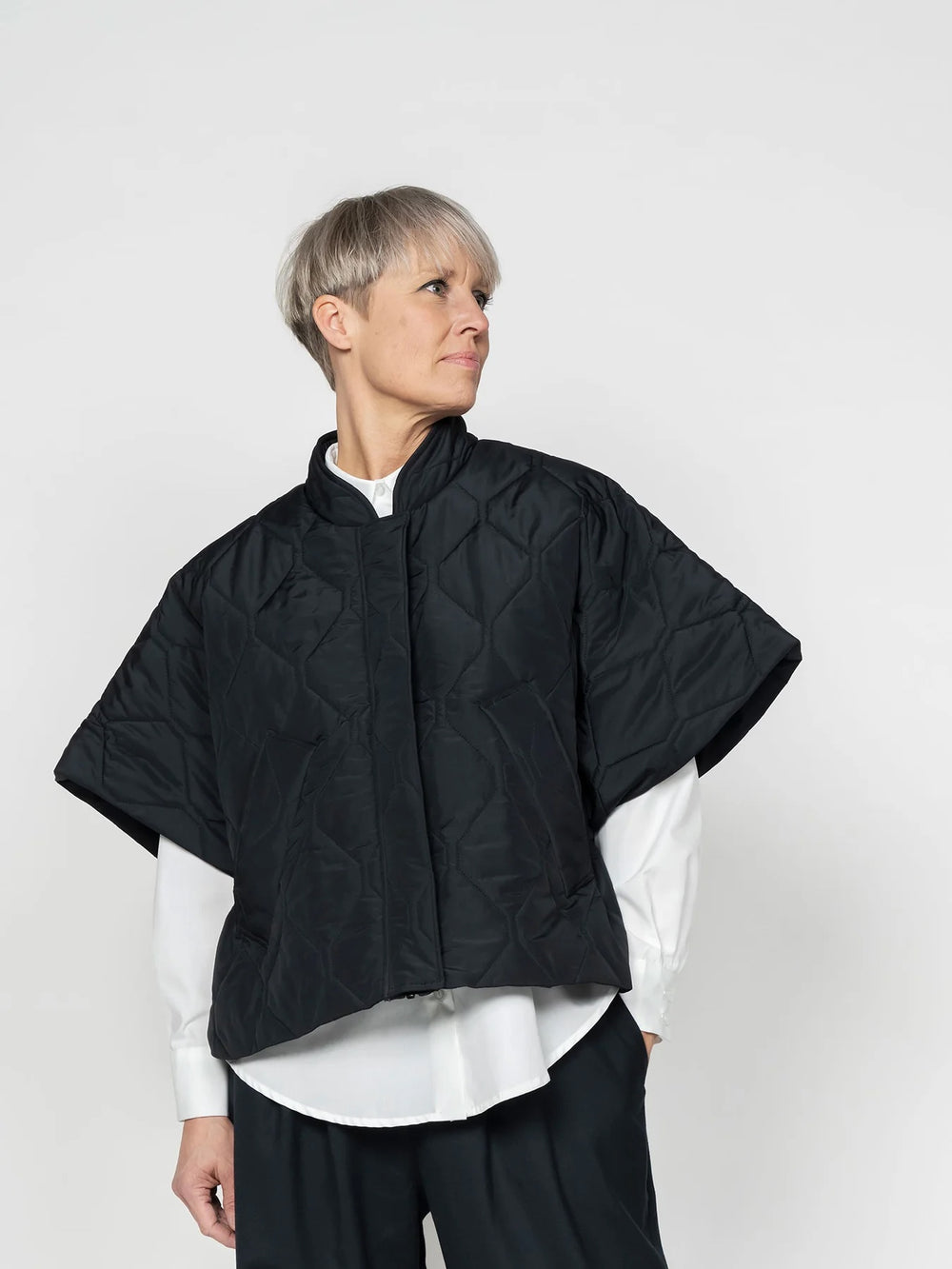 Woman wearing the Drawstring Vest sewing pattern from The Assembly Line on The Fold Line. An outerwear pattern made in pre-quilted fabric, featuring a cropped silhouette, open sides with adjustable drawstring toggles, zip front closure, and welt pockets.