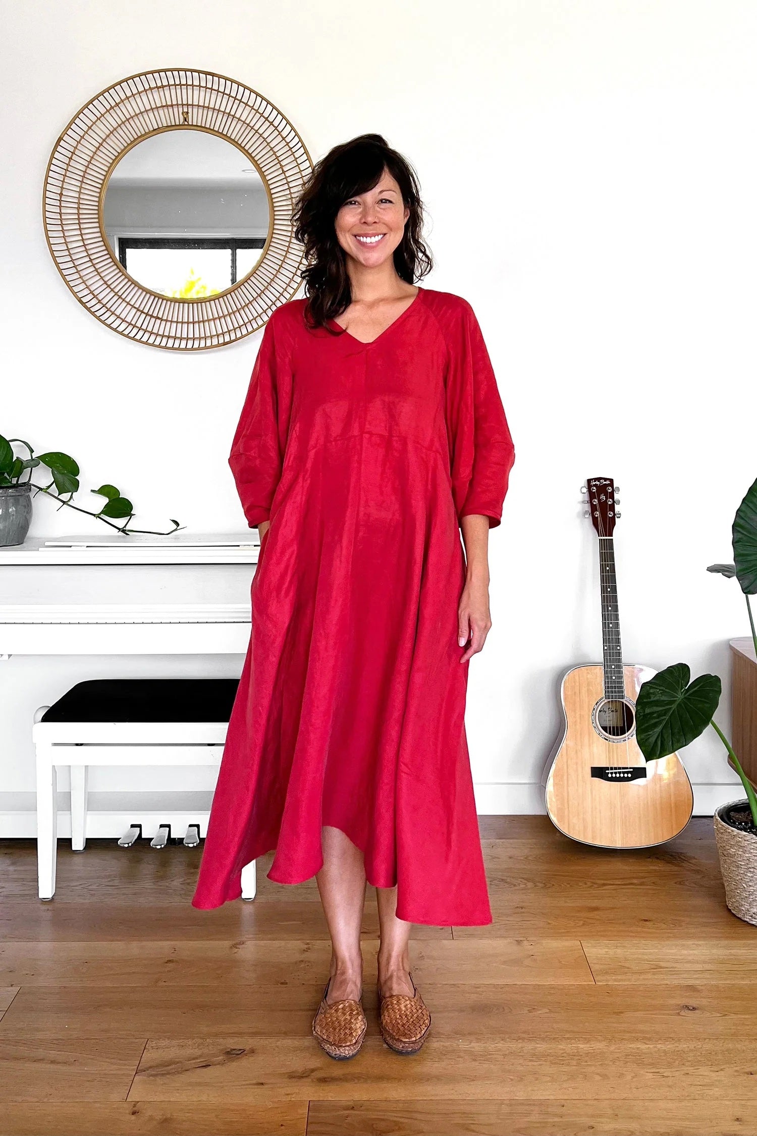 Woman wearing the Elwood Dress sewing pattern from In the Folds on The Fold Line. A dress pattern made in linen, linen blend, cotton poplin, shirting, chambray, sateen, silk (crepe de chine or habotai), double gauze, or viscose (rayon) fabric, featuring a relaxed fit, v-neck, mid-length raglan sleeves with a lantern shape, in-seam pockets, and midi length.
