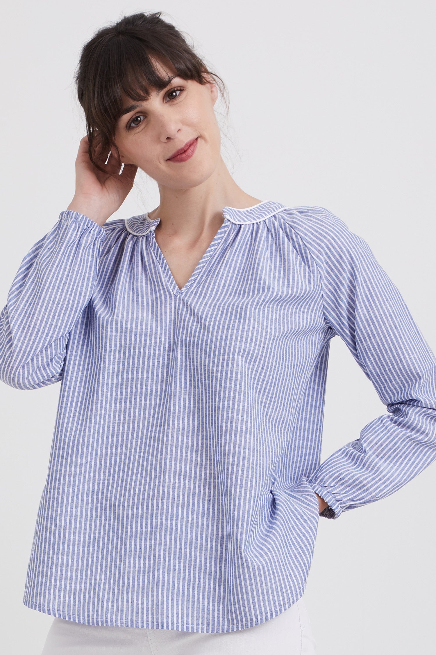 Woman wearing the Estelle Blouse sewing pattern from Coralie Bijasson on The Fold Line. A boho blouse pattern made in cotton, veil, crepe, or viscose fabric, featuring a relaxed fit, gathered neckline, long raglan sleeves, and a shaped hem.
