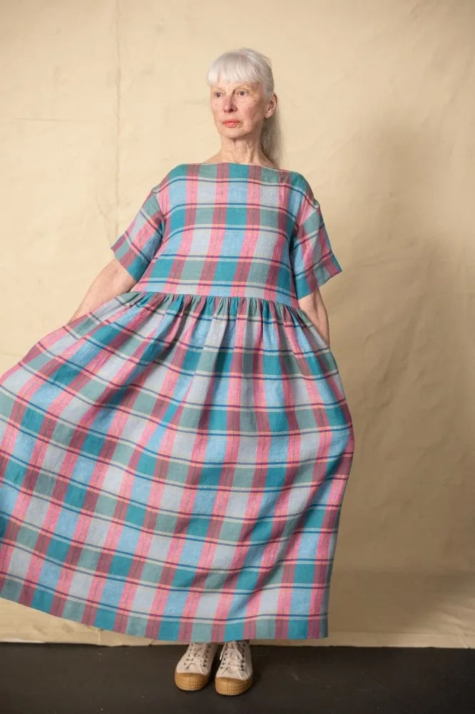 Woman wearing the Factory Dress Boat Neck Addition sewing pattern from Merchant & Mills on The Fold Line. A dress pattern made in linen, linen blends, tencel, cotton chambray, very fine wool or corduroy fabric, featuring a relaxed oversized silhouette, boat neck, short sleeves, gathered skirt, and pockets.