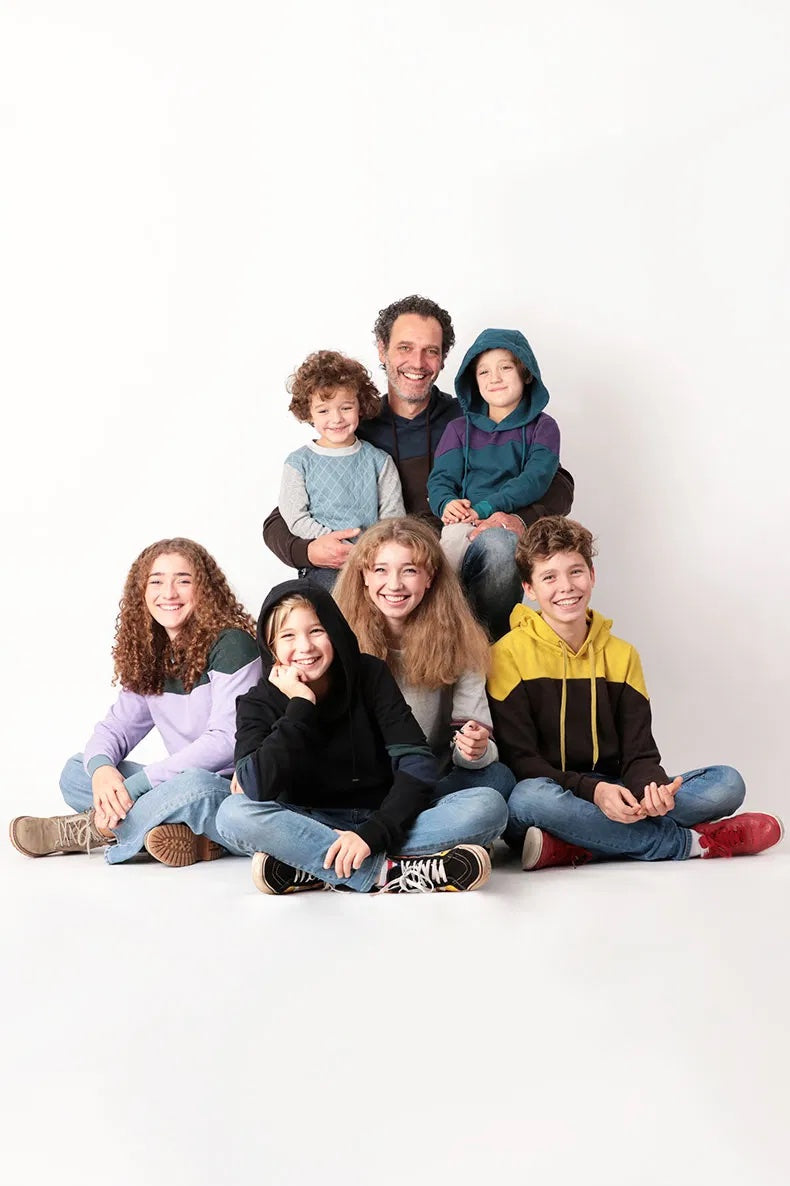 A man, teens, and children wearing the Family Ada Sweatshirt sewing pattern from Schnittchen Patterns on The Fold Line. A sweatshirt pattern made in sweatshirt fabric, featuring a ribbed neckband or hood, long sleeves, and colour blocking options.