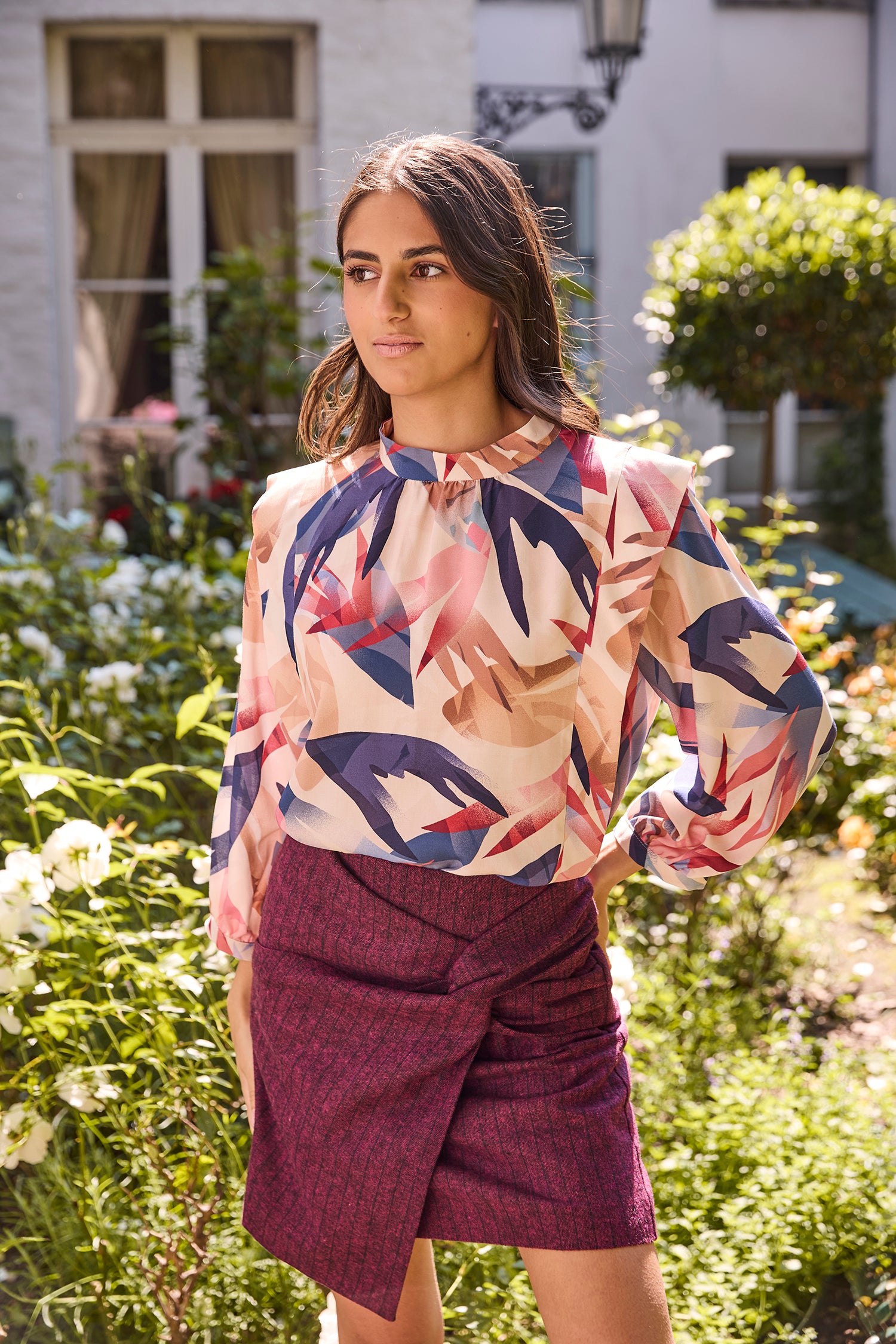 Woman wearing the Gabrielle Blouse sewing pattern from Atelier Jupe on The Fold Line. A blouse pattern made in viscose, cotton, tencel, linen, or non-static polyester fabric, featuring a relaxed fit, gathered neckline with stand-up collar, flounces down the front and back bodice, and long sleeves.