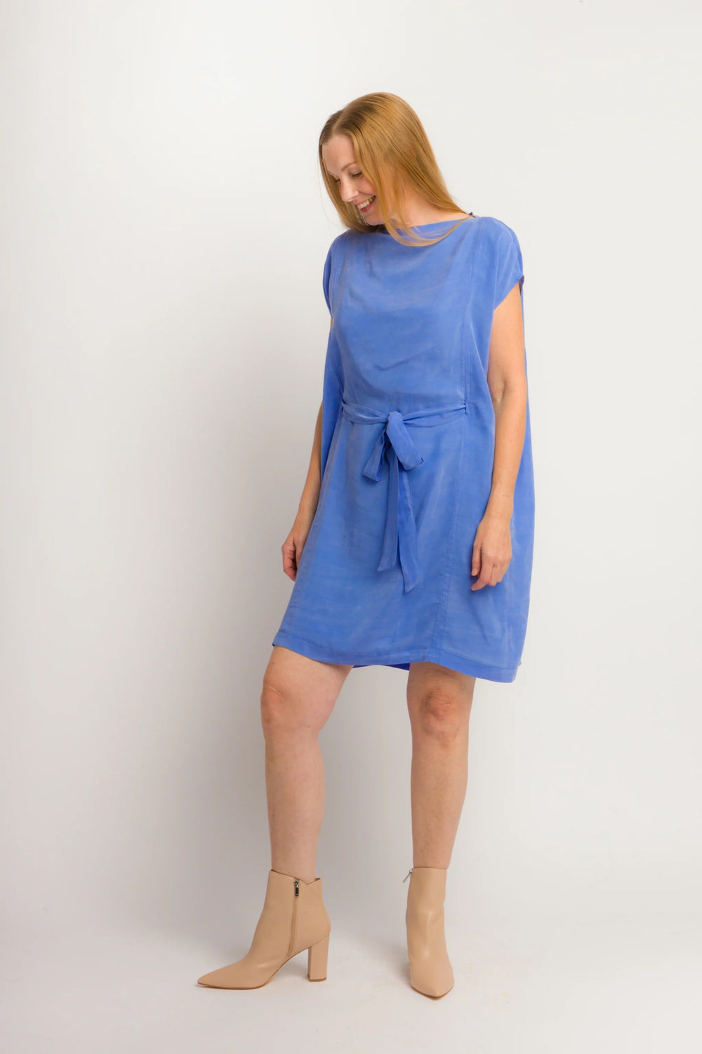 Woman wearing the Gemini Dress sewing pattern from Cris Wood Sews on The Fold Line. A dress pattern made in linen, lightweight cotton, silk, rayon, viscose blend, gauze, or stable knit fabric, featuring a shallow funnel neckline, short grown-on sleeves, a long tie belt, and knee length.