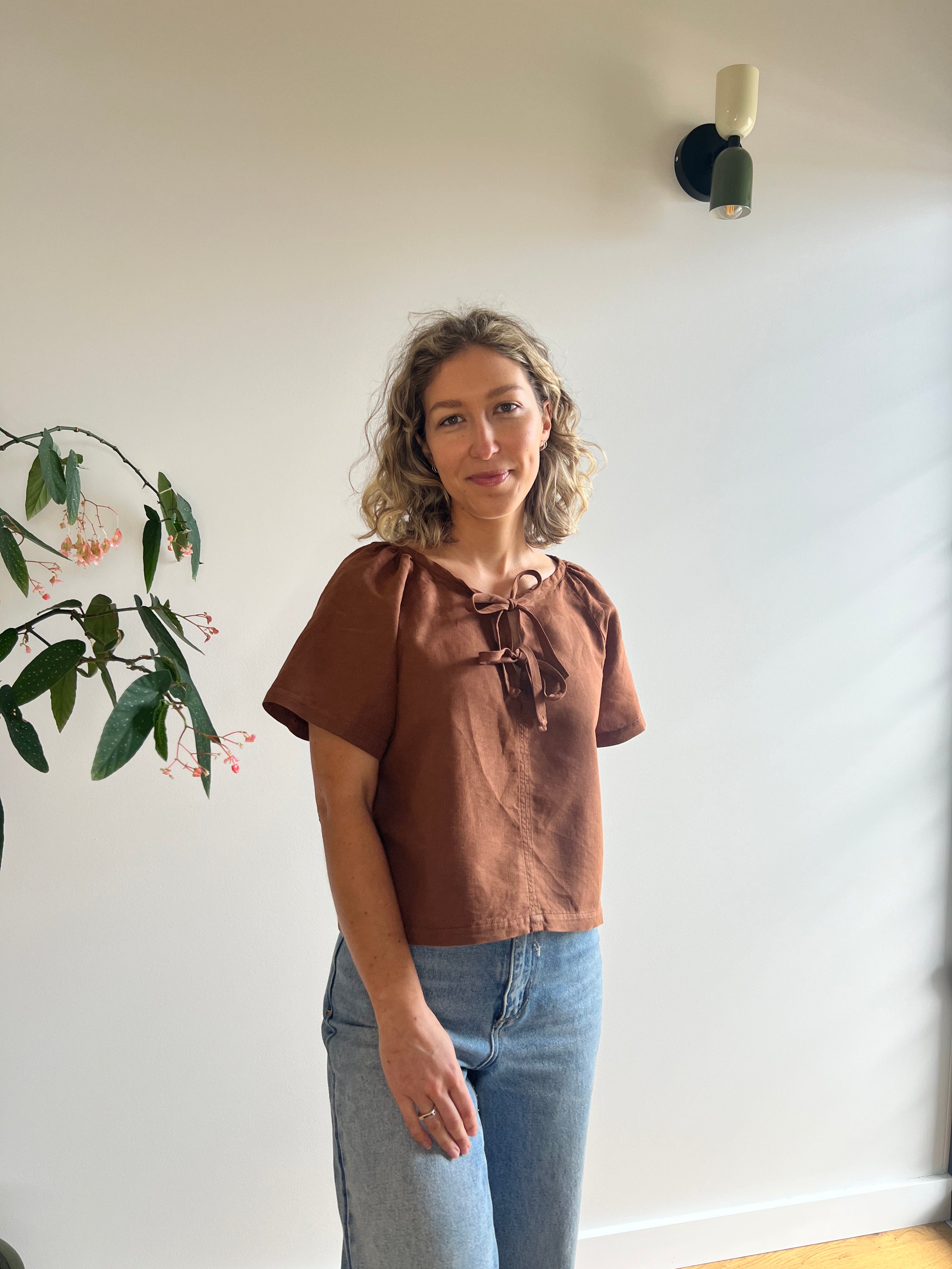 Woman wearing the Ginny Top sewing pattern from Elle Stitch on The Fold Line. A blouse pattern made in cotton, linen, rayon, or seersucker fabric, featuring a relaxed fit, bias bound neckline, tie front, and short raglan sleeves.
