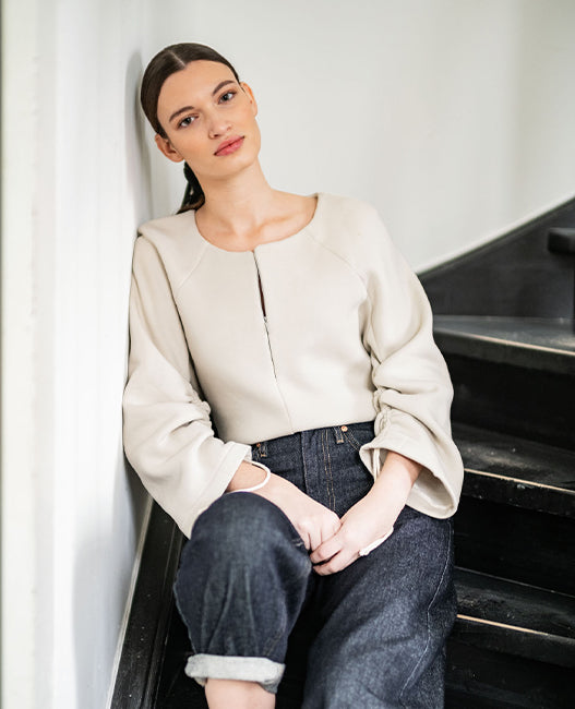 Woman wearing the Gitika Jumper sewing pattern from Fibre Mood on The Fold Line. A top pattern made in ribbed jersey, French terry, scuba, interlock, knitted jacquard, fine or coarse knit, sweater fabric, or velvet, featuring a round neck, concealed front zip, and long raglan sleeves with drawstrings.