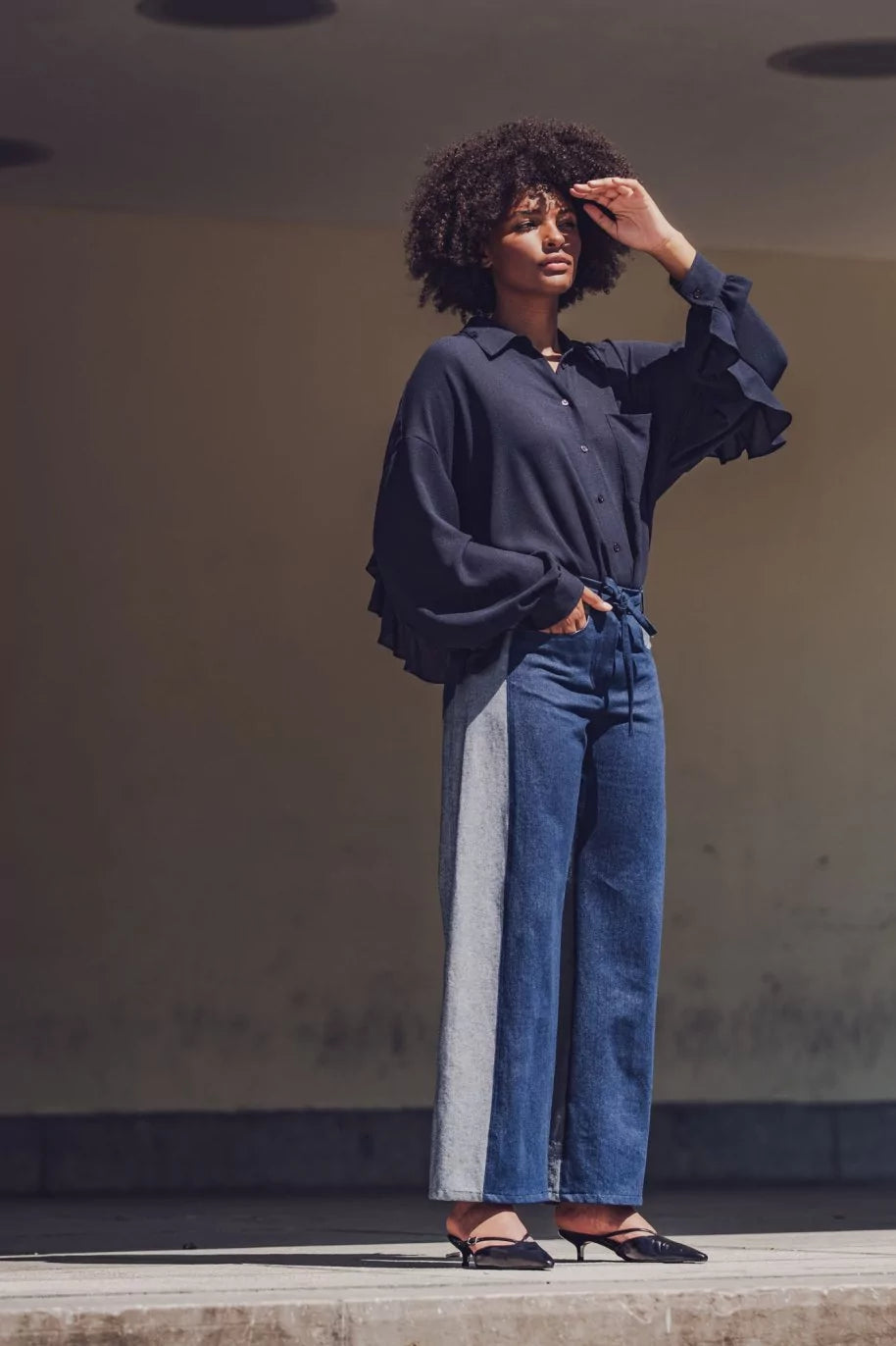 Woman wearing the Johanna Trousers sewing pattern from Fibre Mood on The Fold Line. A trousers pattern made in denim, corduroy, cotton twill, leather, or woven jacquard fabric, featuring a straight waistband with belt loops and a tie, zip fly, side panels, coin pocket, curved front pockets, and pointed back pockets.