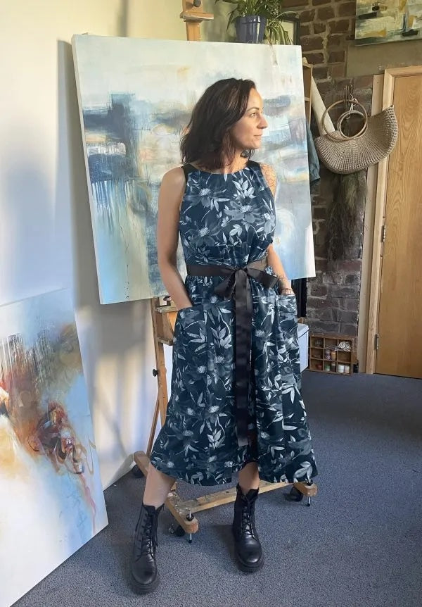 Woman wearing the Kahlo Tabard sewing pattern from Sew Different on The Fold Line. A sleeveless wrap dress pattern made in cotton, linen, denim, needlecord, or wool fabric, featuring a lined bodice, oversized pockets, and a grosgrain ribbon waist tie.
