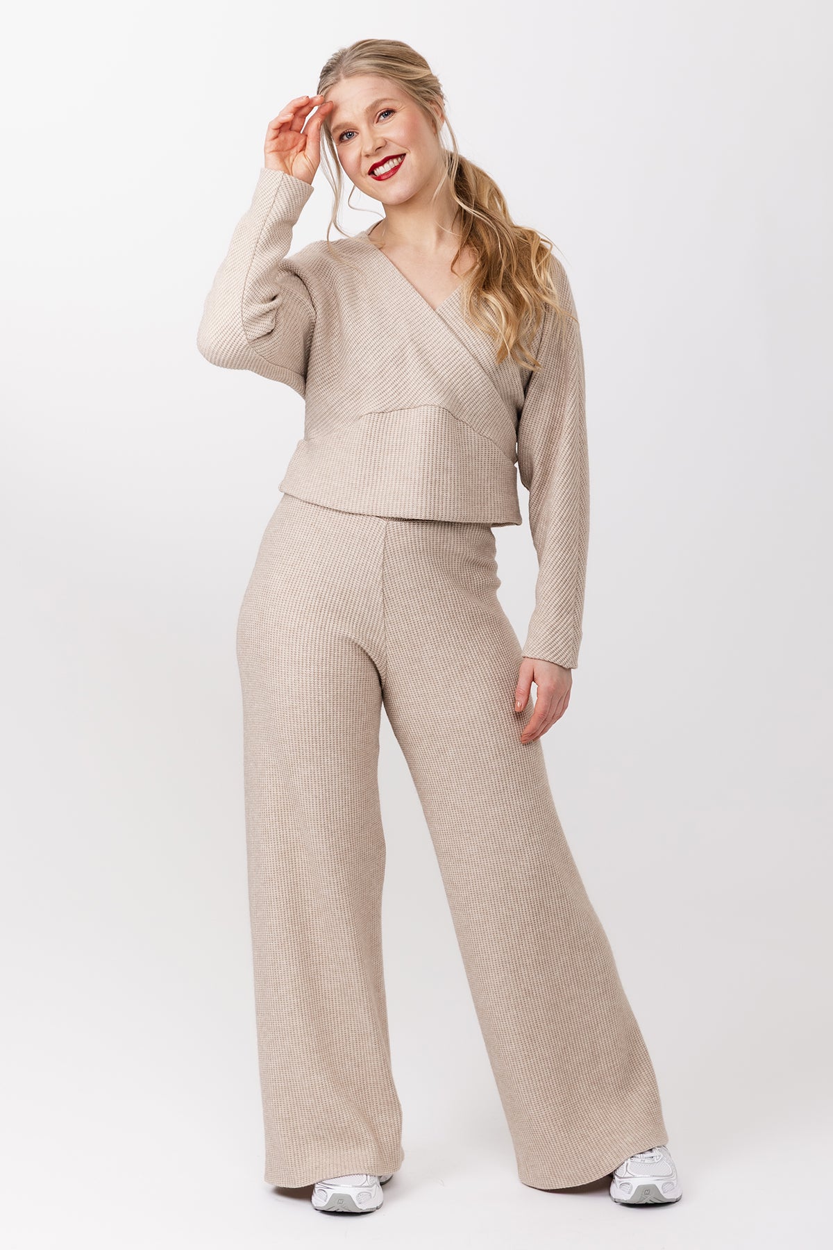 Woman wearing the Kajo Wrap Sweater and Olo Pants sewing pattern bundle from Named on The Fold Line. Top and pants patterns made in knit fabric, featuring a relaxed fit, V-neck, long batwing sleeves, and curved hem band for the top and elasticated waist and wide leg for the pants.