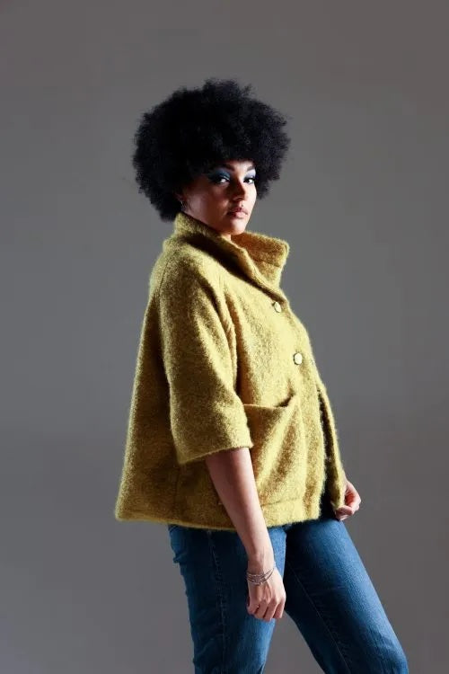 Woman wearing the Kusama Jacket sewing pattern from Sew Different on The Fold Line. A lined jacket pattern made in denim, boiled wool, heavy cotton, bouclé, felt, scuba, heavy linen, corduroy, velvet, twill, or tweed fabric, featuring an oversized shape, funnel neck, half-length raglan sleeves, patch pockets, and snaps.