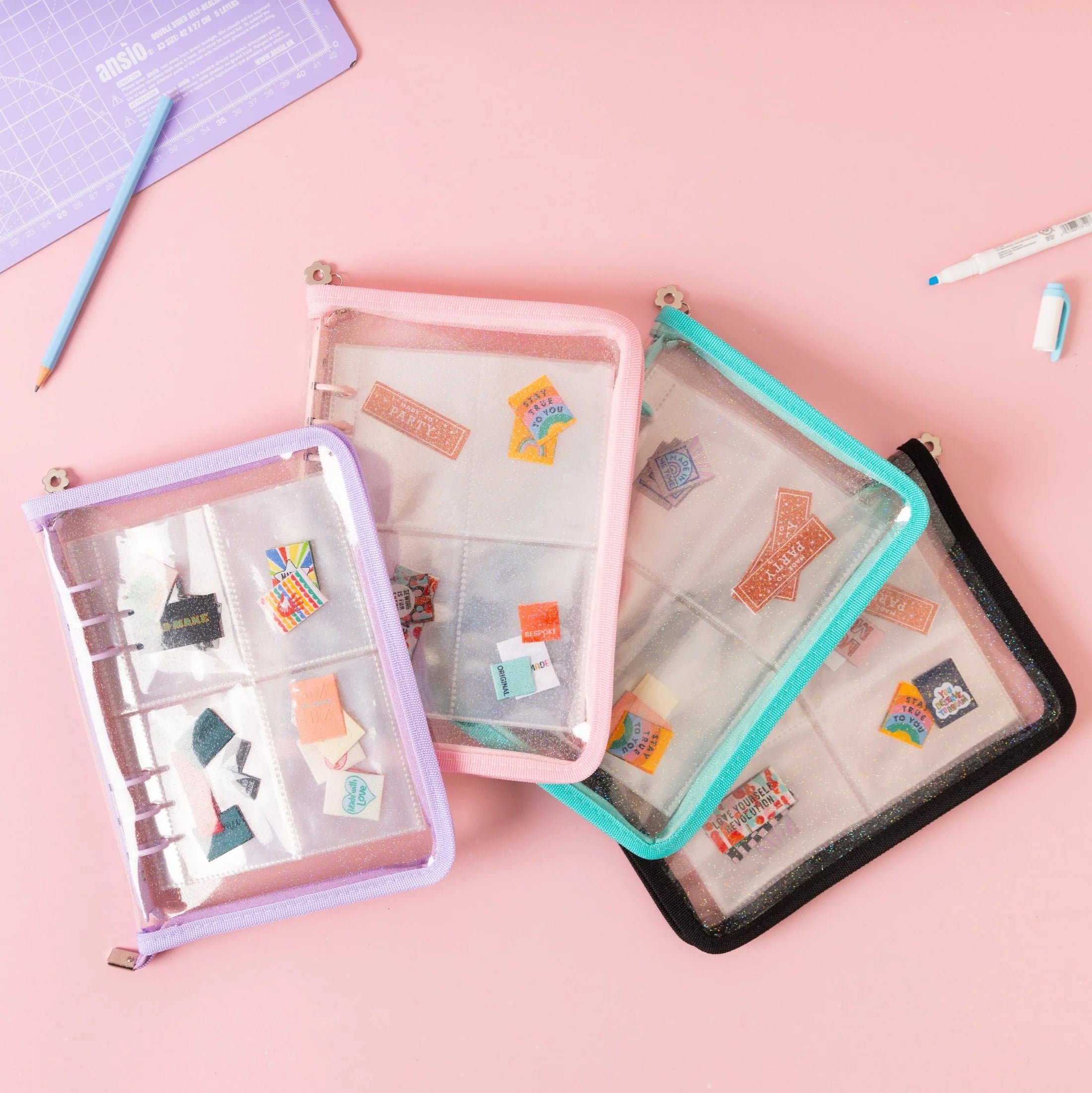 The Label Stash Folder from Little Rosy Cheeks on The Fold Line. A glittery transparent folder for organising your labels, featuring sleeves with pockets and a zipper closure.