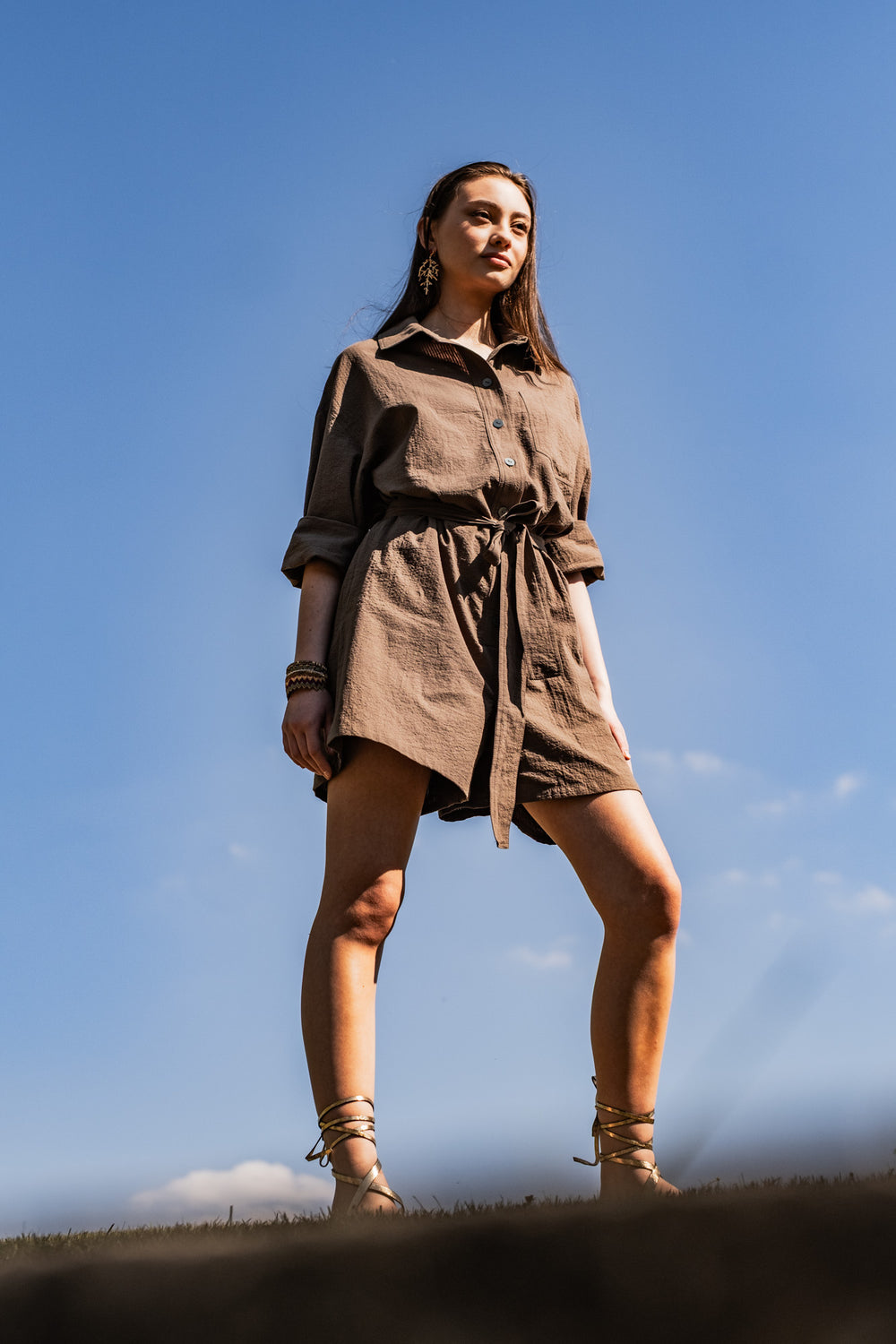 Woman wearing the Liberty Playsuit sewing pattern from Fibre Mood on The Fold Line. A playsuit pattern made in cotton twill, poplin, fine corduroy, or linen fabric, featuring an oversized fit, shirt collar, front button placket, long sleeves with cuffs, chest pocket, tie belt, and shorts length.