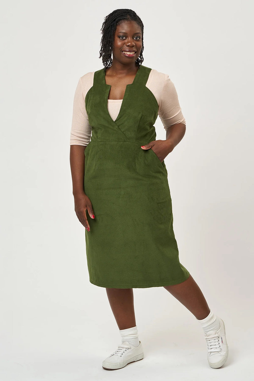 Woman wearing the Lorna Pinafore sewing pattern from Sew Over It on The Fold Line. A pinafore dress pattern made in denim, cotton poplin, cotton canvas, brocade, suiting, gabardine, or wool fabric, featuring a notched bodice, wide straps, straight skirt, pockets, and midi length.