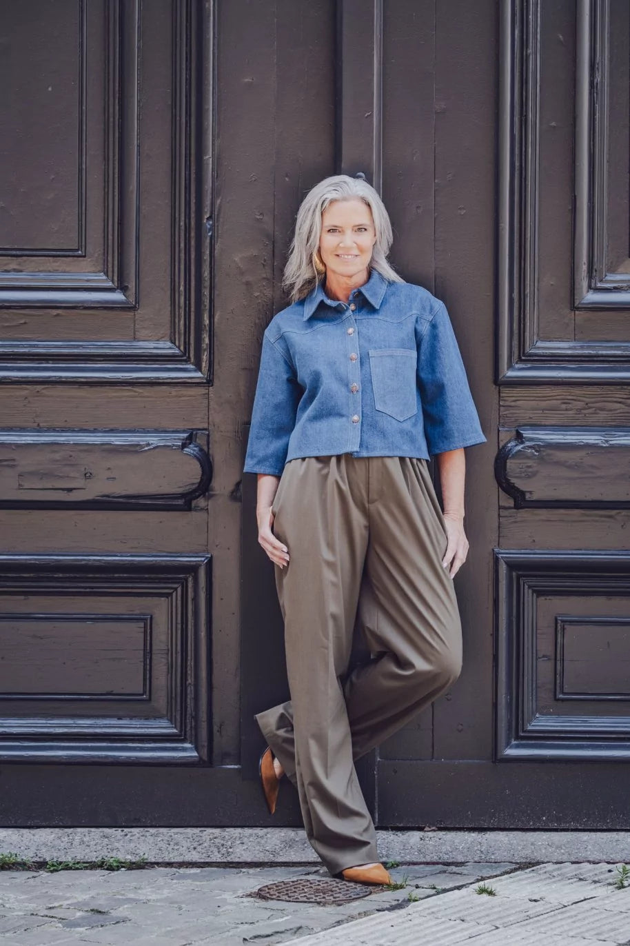 Woman wearing the Melody Shirt sewing pattern from Fibre Mood on The Fold Line. A shirt pattern made in denim, poplin, textured cotton, fine corduroy, woven jacquard, chambray, or satin fabric, featuring a boxy shape, collar, button front, chest pocket, short sleeves, and cropped length.