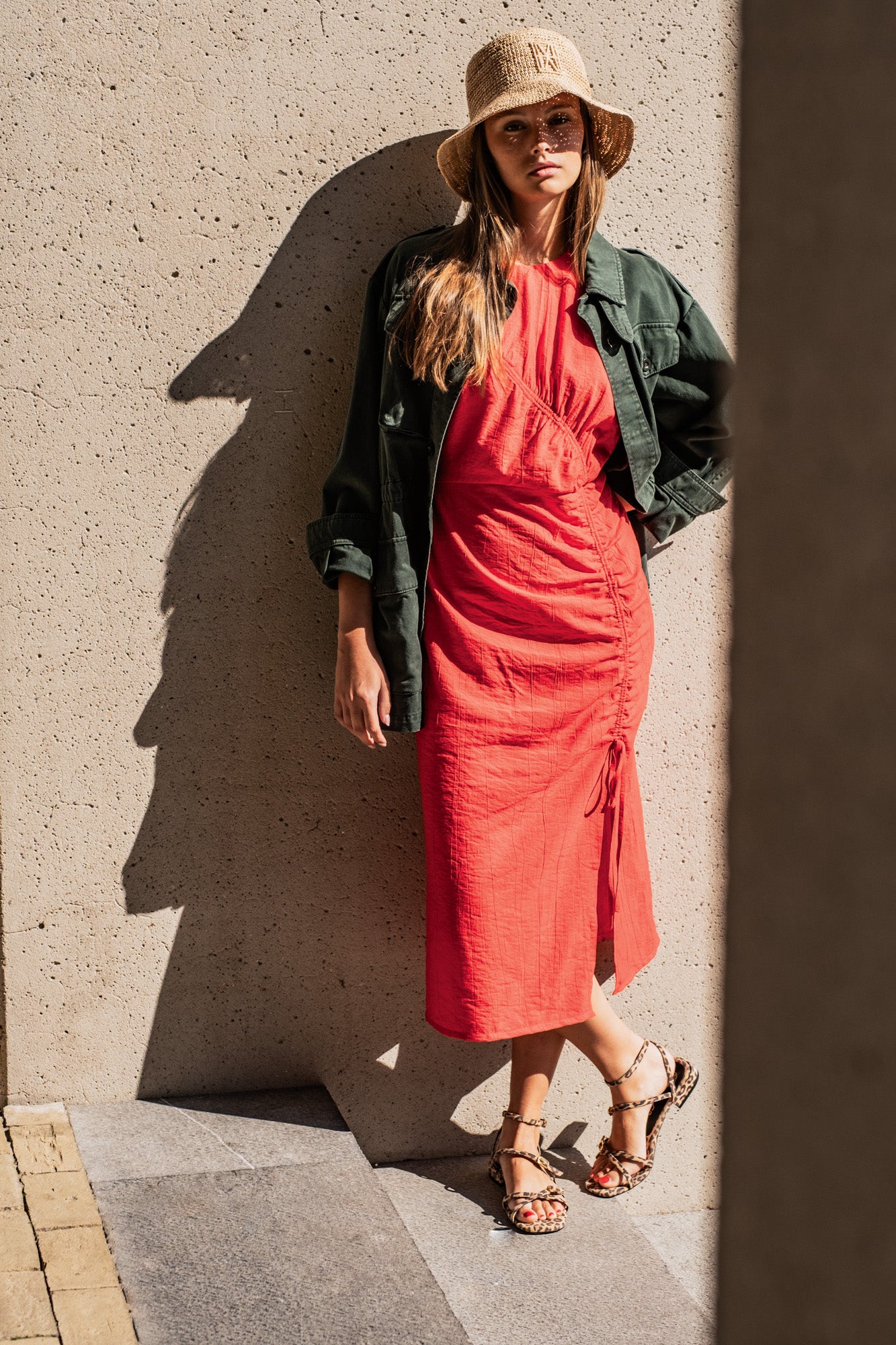 Woman wearing the Muriel Dress sewing pattern from Fibre Mood on The Fold Line. A sleeveless dress pattern made in poplin, linen, twill, double gauze, chambray, seersucker, or dobby fabric, featuring a fitted silhouette, round neckline, gathered channel from the bust to the front slit, and midi length.