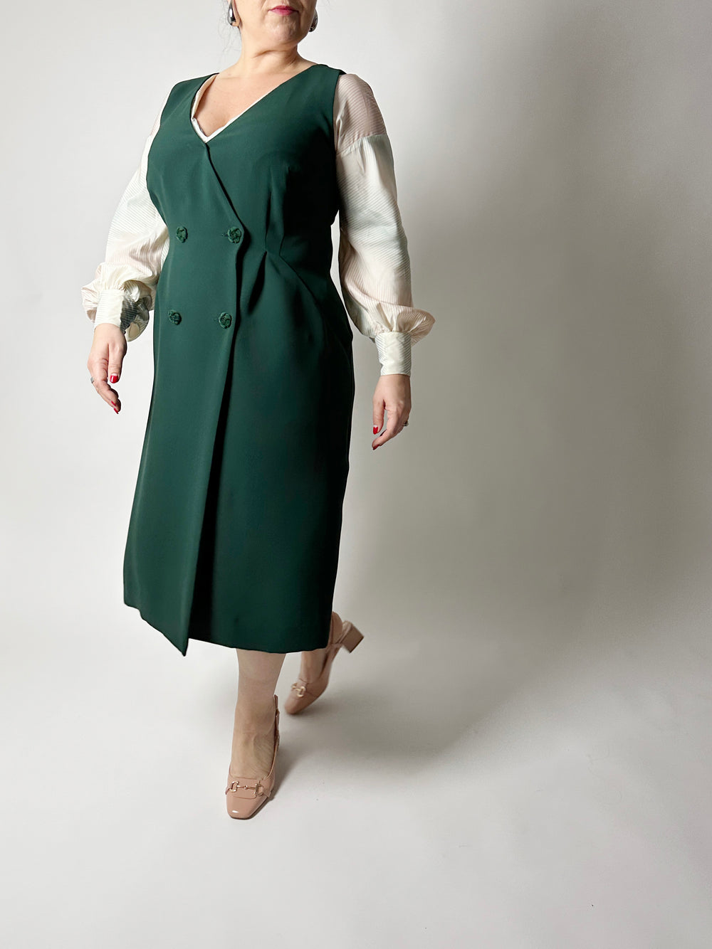 Woman wearing the No. 33 Lissabon Dress sewing pattern from How to Do Fashion on The Fold Line. A vintage-inspired sleeveless dress pattern made in cotton, silk, wool, viscose, cupro, linen, or polyester fabric, featuring a deep V-neckline, double-breasted button front, and midi length.