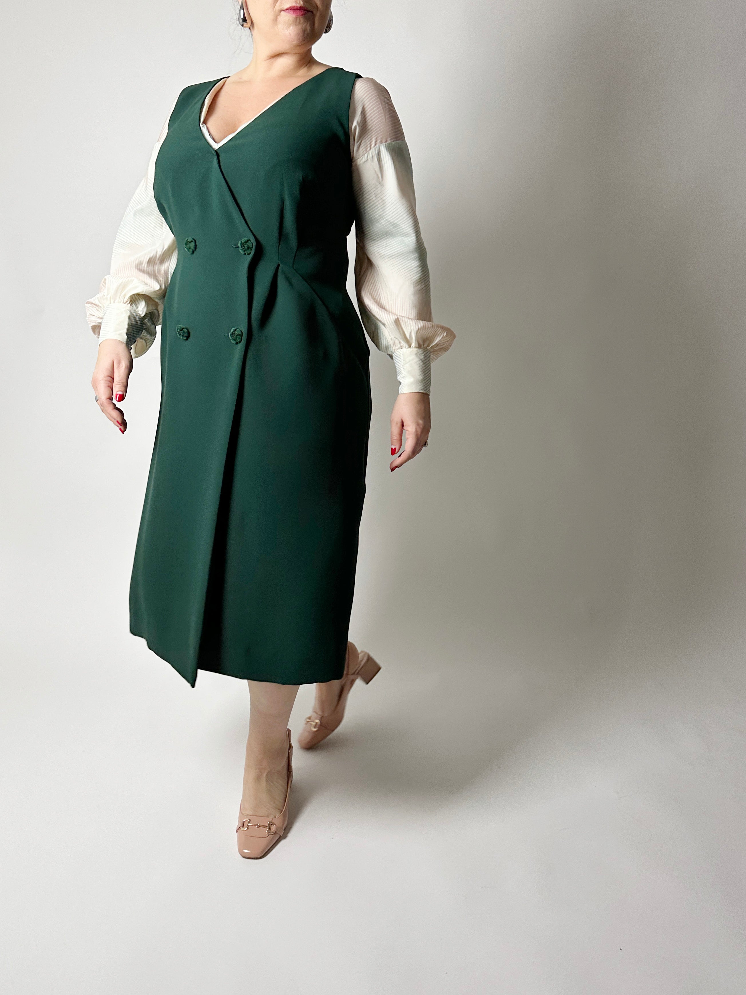 Woman wearing the No. 33 Lissabon Dress sewing pattern from How to Do Fashion on The Fold Line. A vintage-inspired sleeveless dress pattern made in cotton, silk, wool, viscose, cupro, linen, or polyester fabric, featuring a deep V-neckline, double-breasted button front, and midi length.