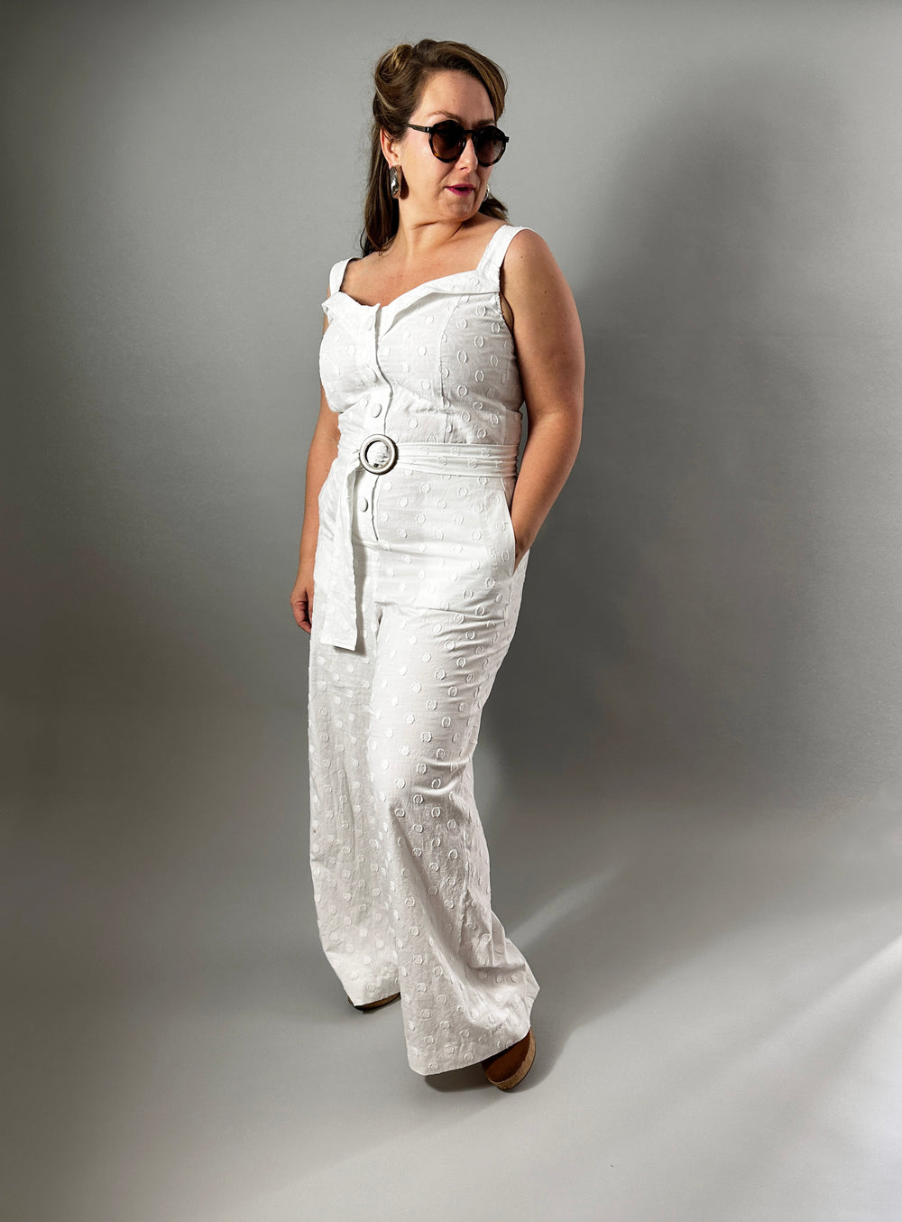 Woman wearing the No. 34 San Marino Jumpsuit sewing pattern from How to Do Fashion on The Fold Line. A jumpsuit pattern made in cotton, silk, wool, viscose, cupro, linen, or polyester fabric, featuring wide shoulder straps, a button placket at the front, elastic shirring at the back, and wide legs with welt pockets.